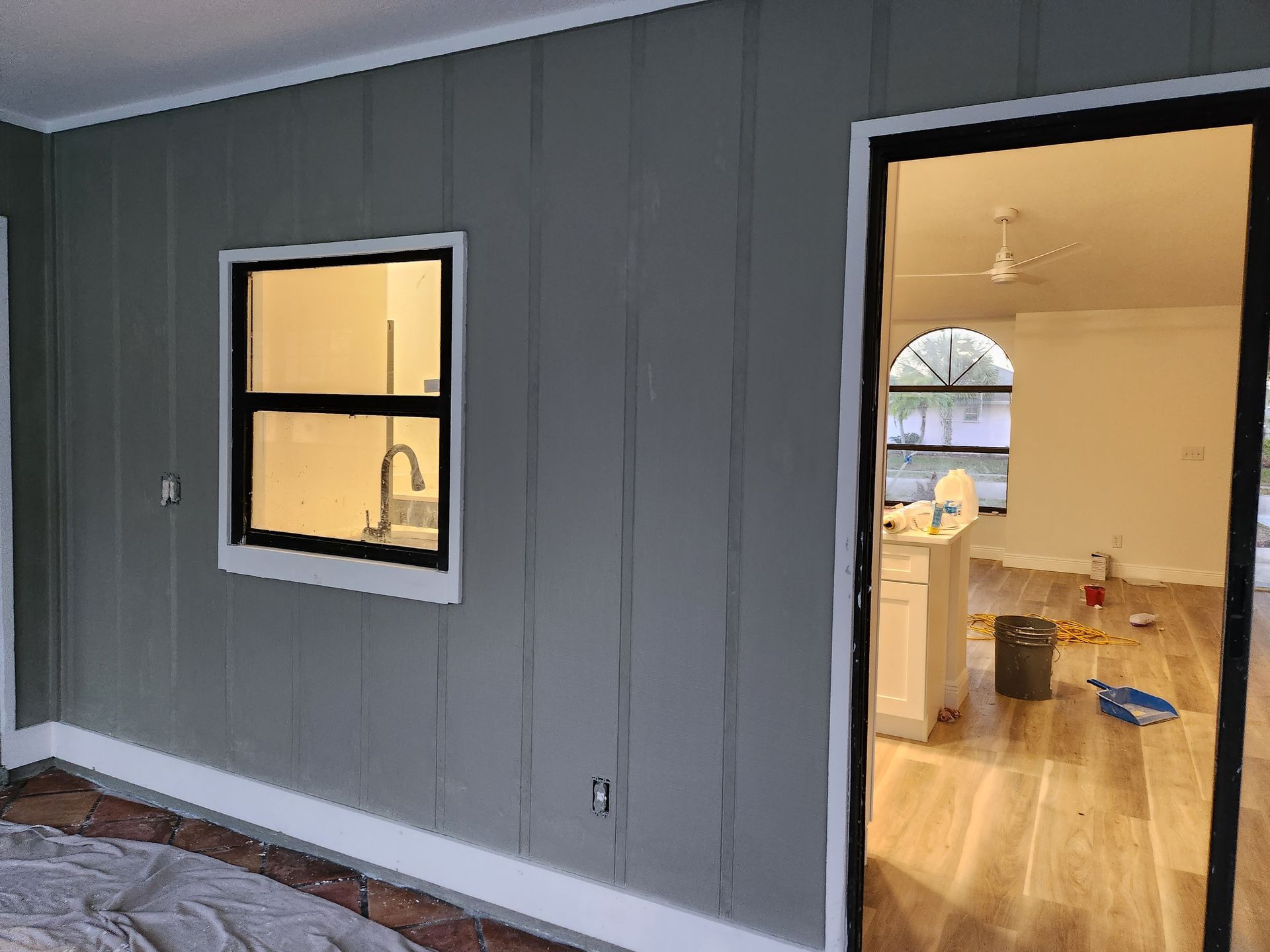 Gray paneled walls with a window and doorway leading into a room with wood flooring, and a cabinet.