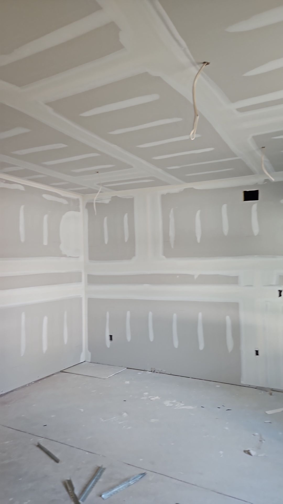 Interior of a room under construction, with drywall walls and ceiling, light fixture, and debris on the floor.