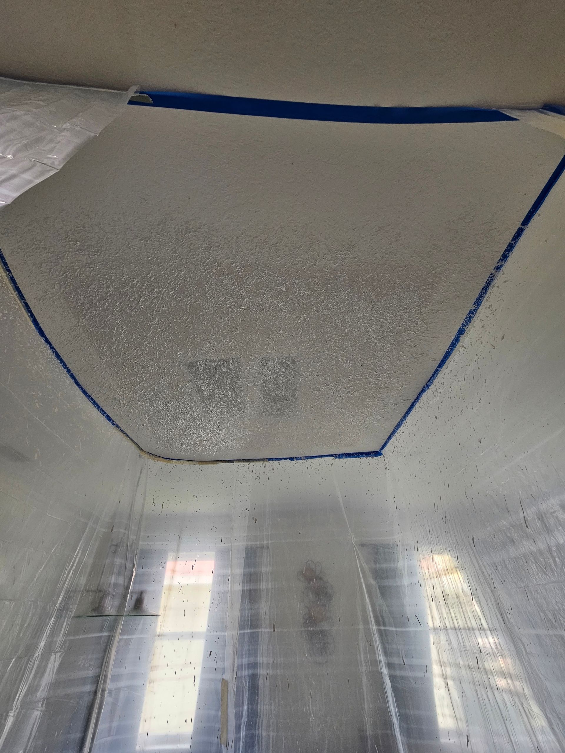 Ceiling partially covered with plastic and taped with blue painter's tape; a hexagonal shape is outlined.