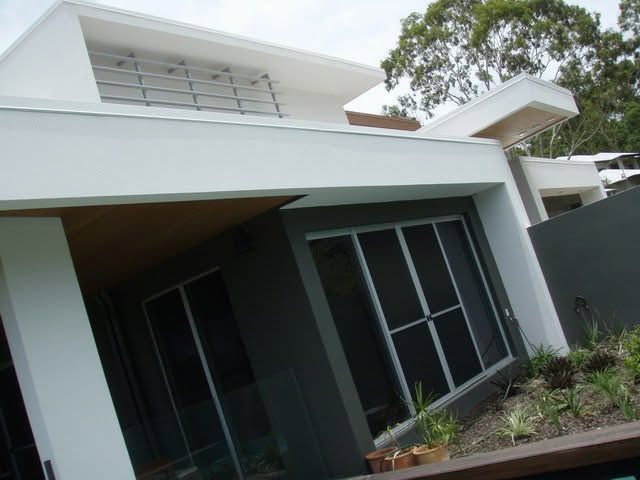 Modern white house with dark windows, a slanted roof, and a small garden in front