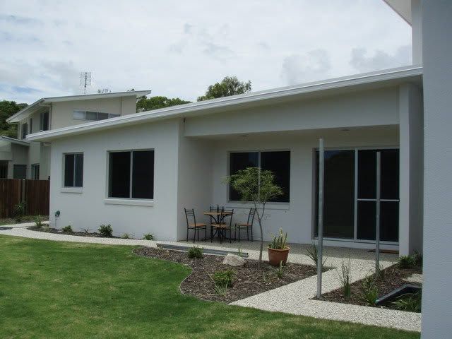 Single-story white house with a small patio, lawn, and sliding glass doors