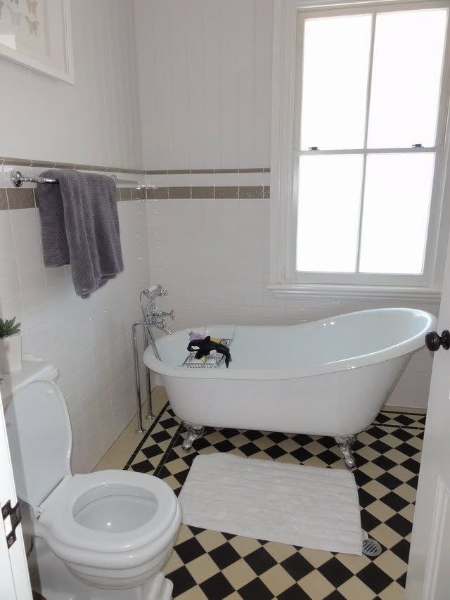 Bright bathroom with black-and-white floor, clawfoot tub, toilet, and window.