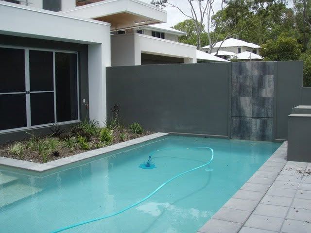 Modern house patio with a turquoise swimming pool and gray privacy wall