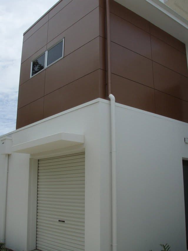 Modern two-story house exterior with brown upper siding and a white garage door