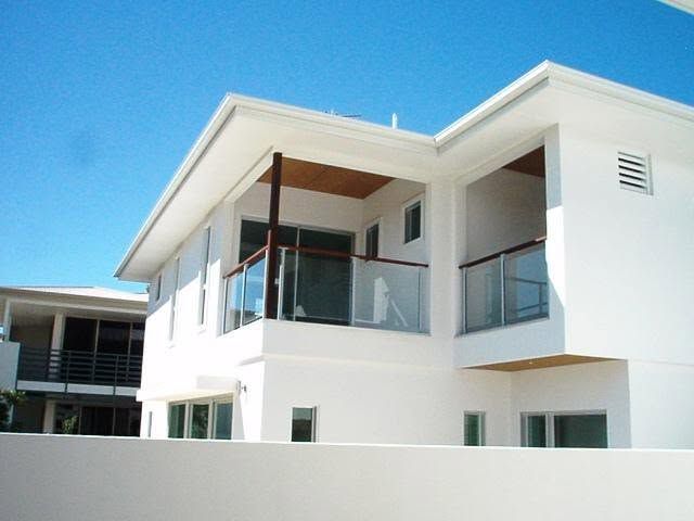 Modern white two-story house with balconies and glass railings under a blue sky