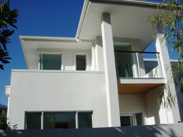 Modern white two-story house with large windows and a balcony under a clear blue sky