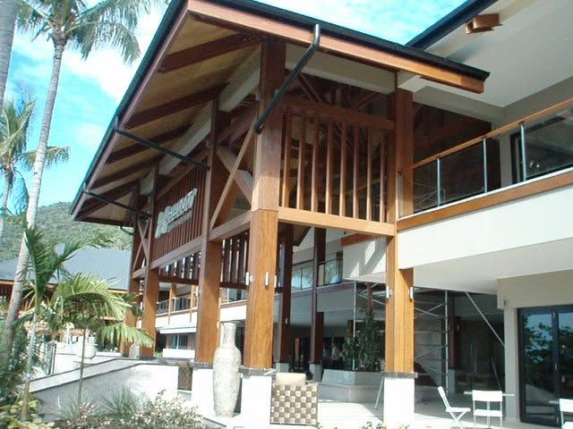 Modern tropical resort building with wood beams, glass balcony, and palm trees outside