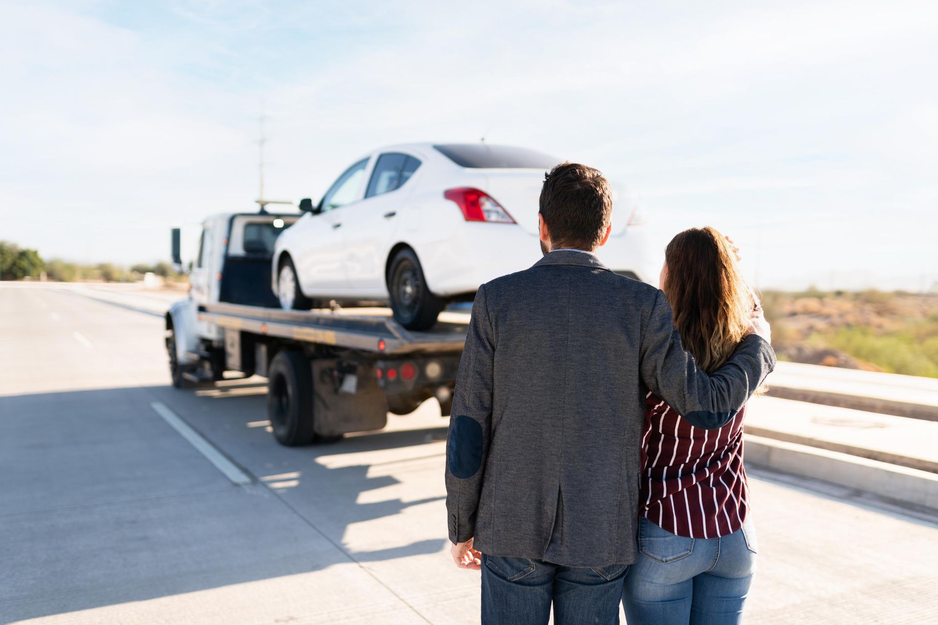 A man and a woman are standing next to a tow truck with a car on it.