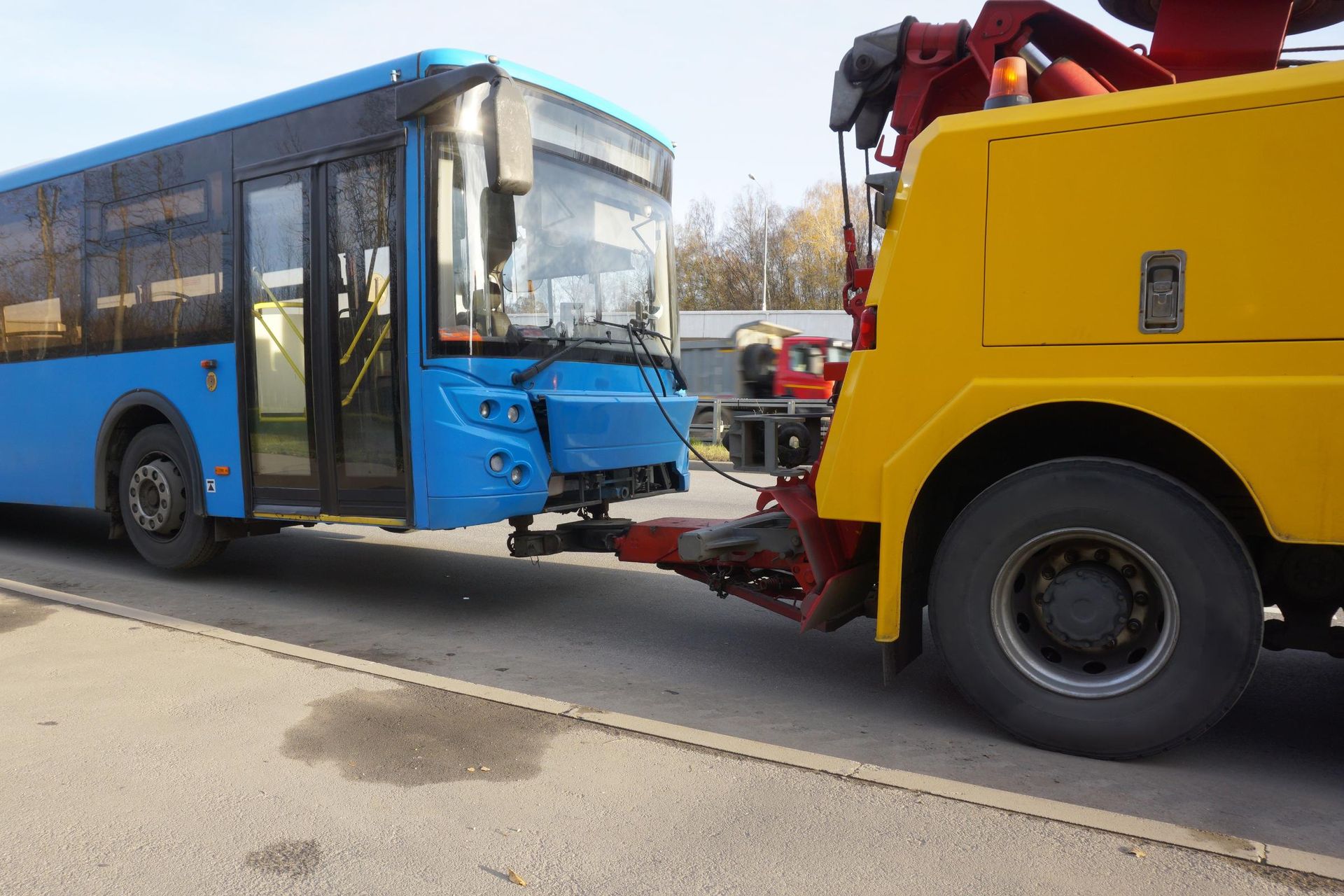 A blue bus is being towed by a yellow tow truck.