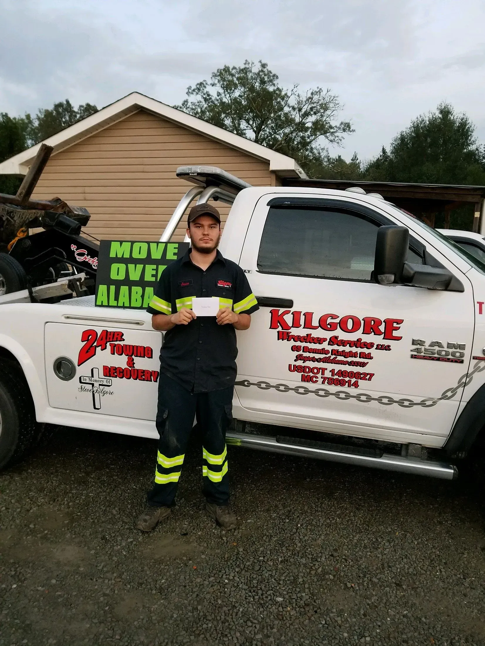 A man is standing in front of a tow truck holding a check.