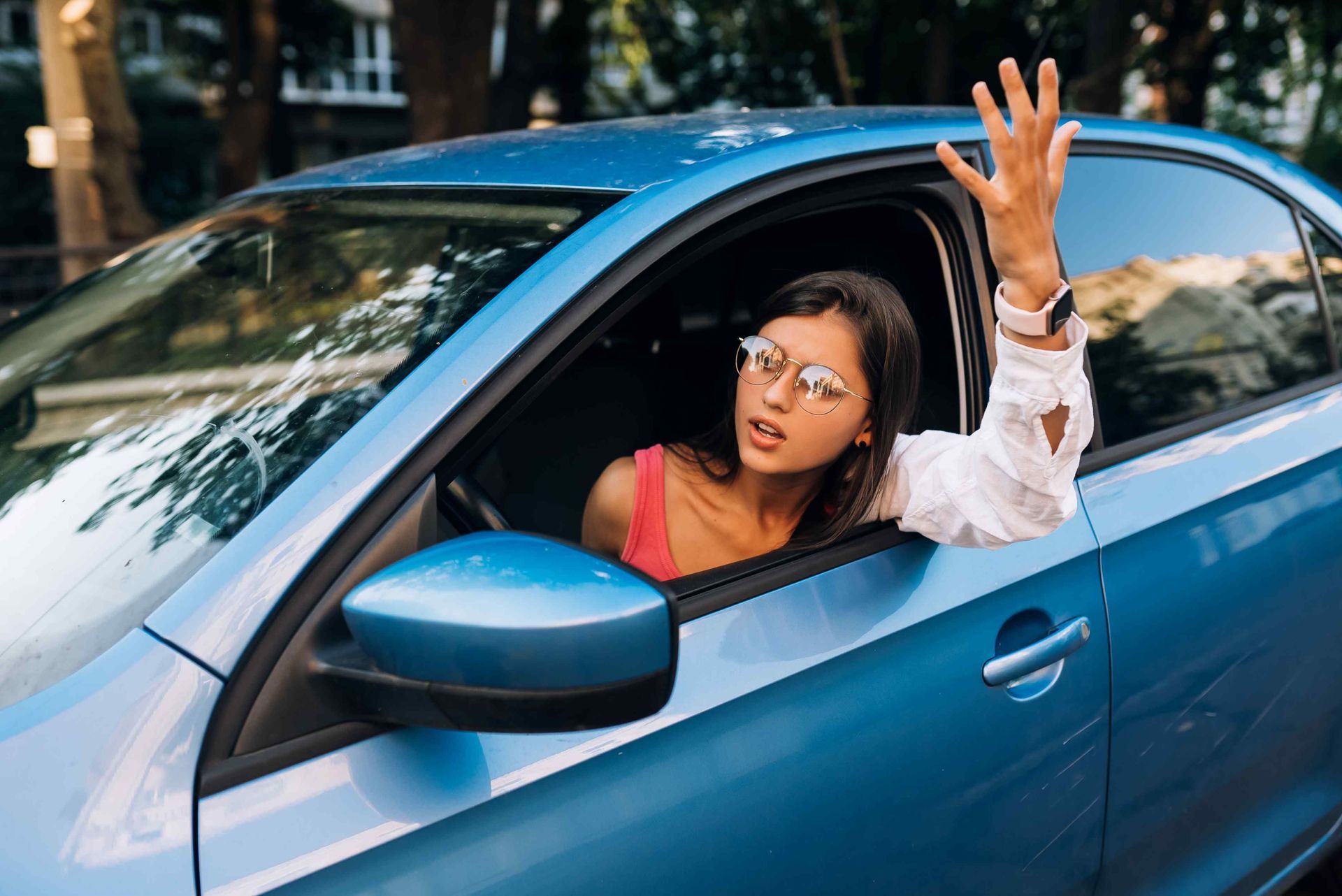 A female driver leaning out of the driver-side window with her hand raised wondering what happened. Clicking this picture takes you to Hit and Run Accidents.