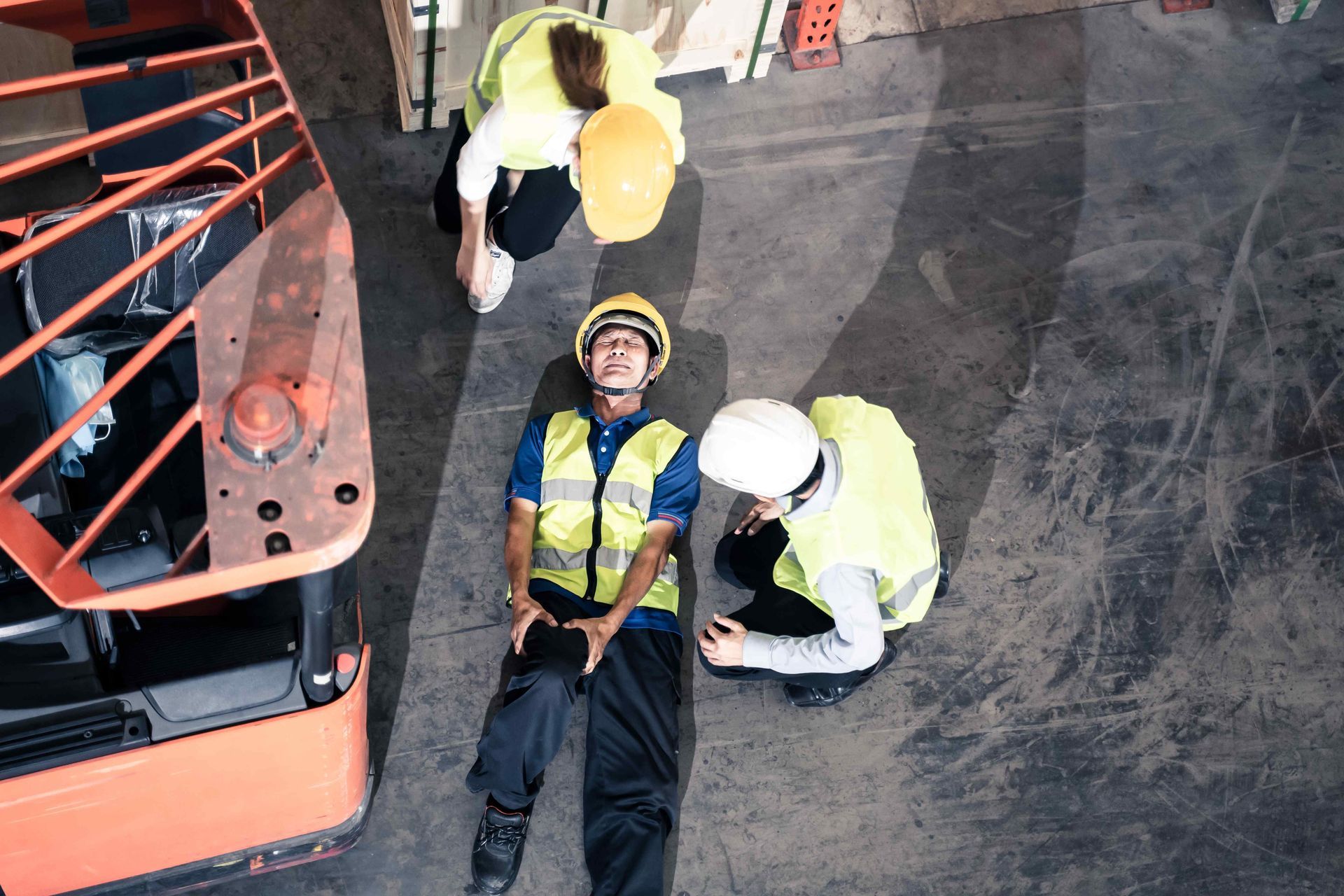 A worker lying on the ground holding their knee close to them, surrounded by two other workers after getting injured in the workplace. Clicking this picture takes you to Workplace Accidents.