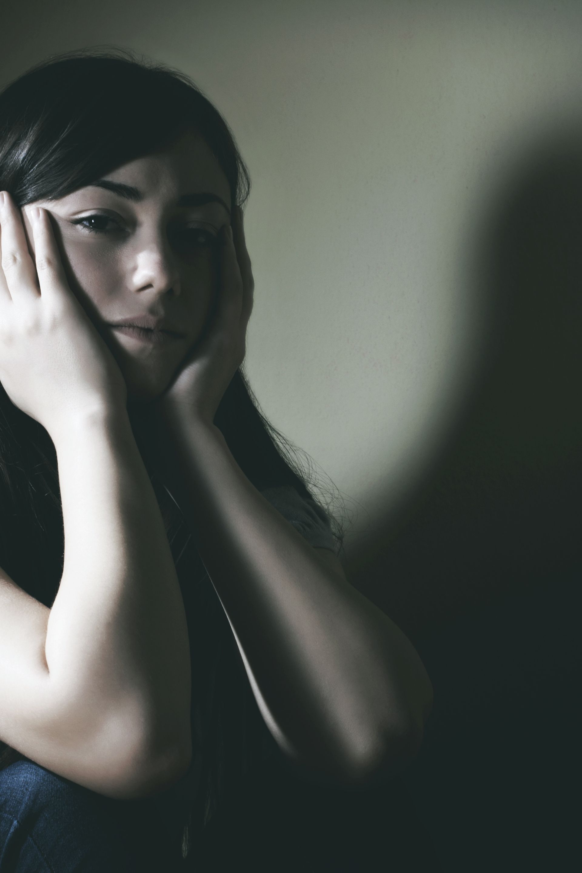Close-up of a young woman holding her face, expressing sadness and emotional distress in a quiet setting