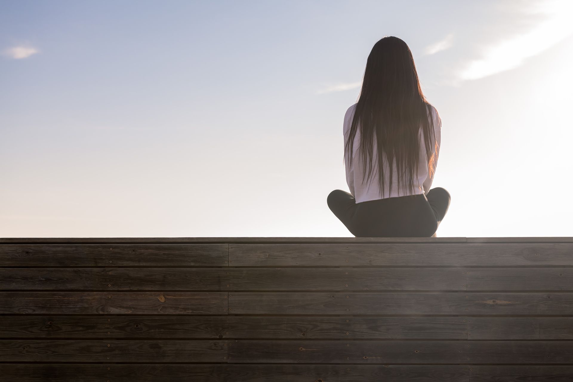 Woman sitting cross-legged from behind, meditating outdoors and focusing on healing and recovery