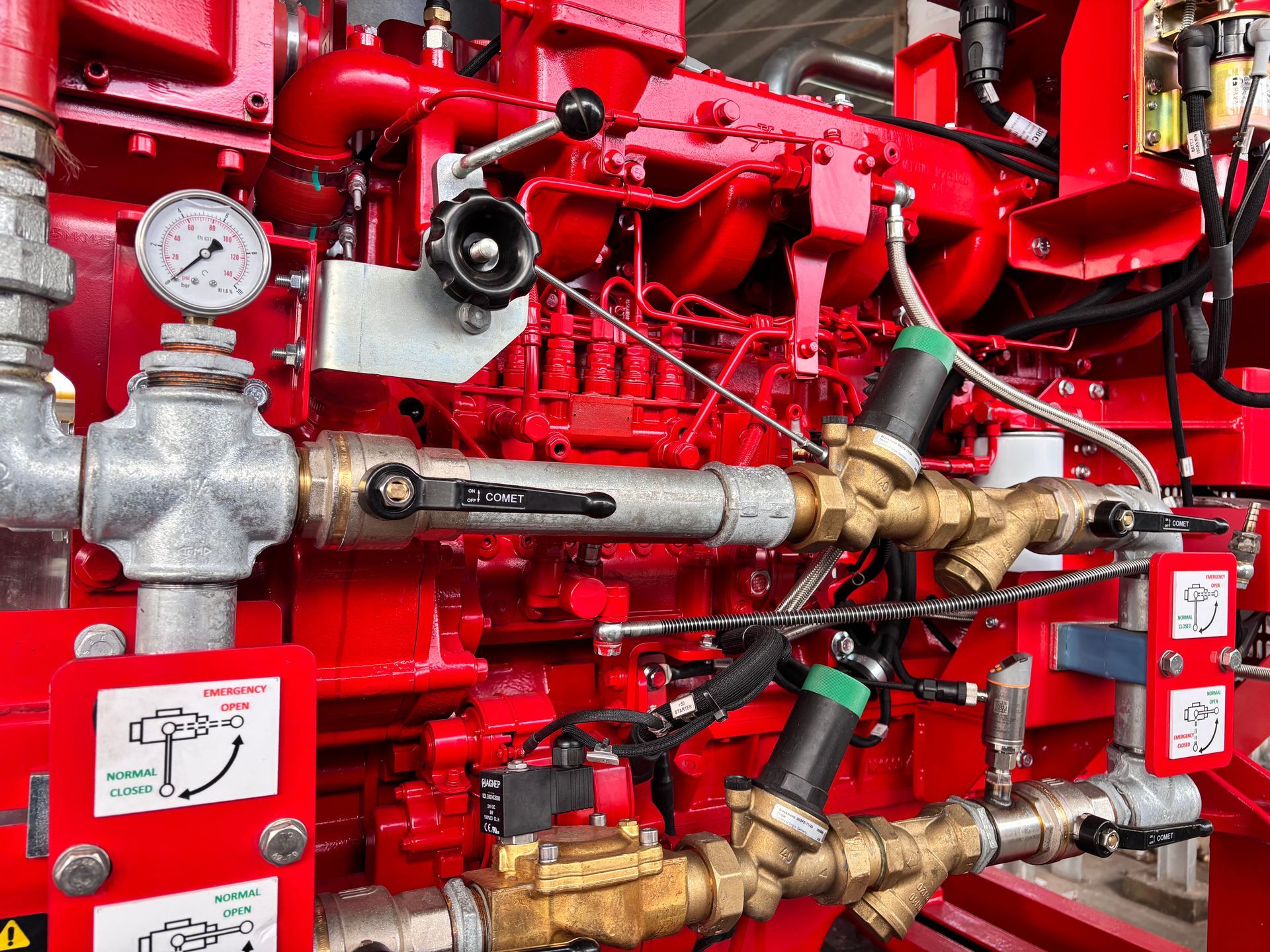 A close-up of a red industrial fire pump engine with silver pipes, pressure gauges, and control valves.