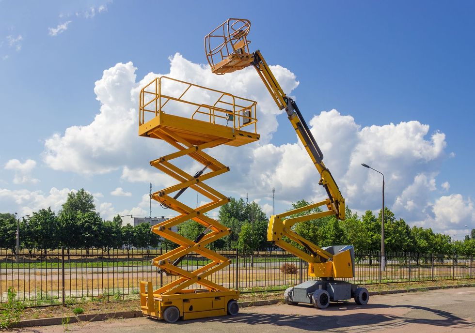 Two yellow aerial work platforms, a scissor lift and an articulating boom lift, parked outdoors under a cloudy blue sky.