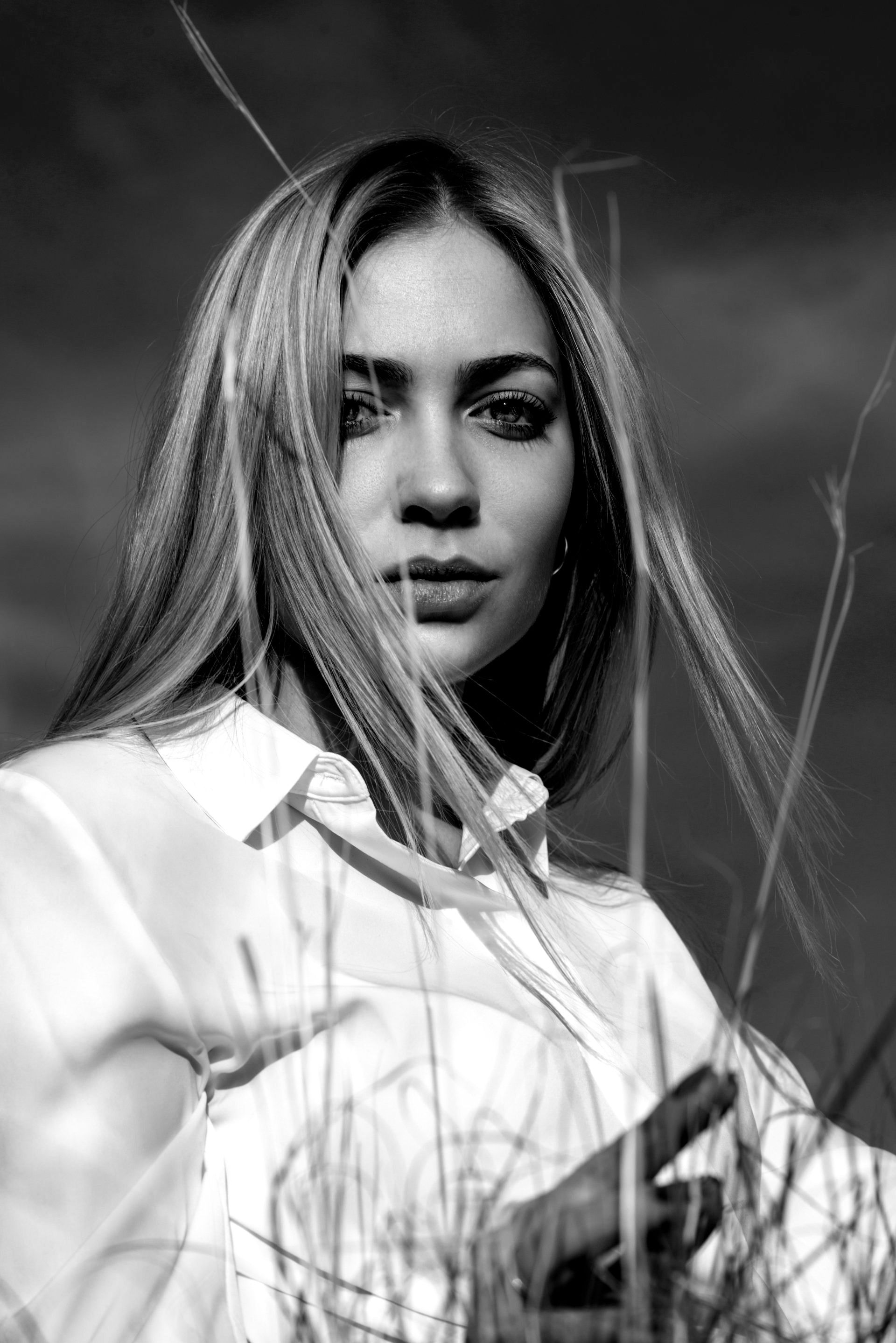 Uma foto em preto e branco de uma mulher em um campo com o cabelo balançando ao vento.