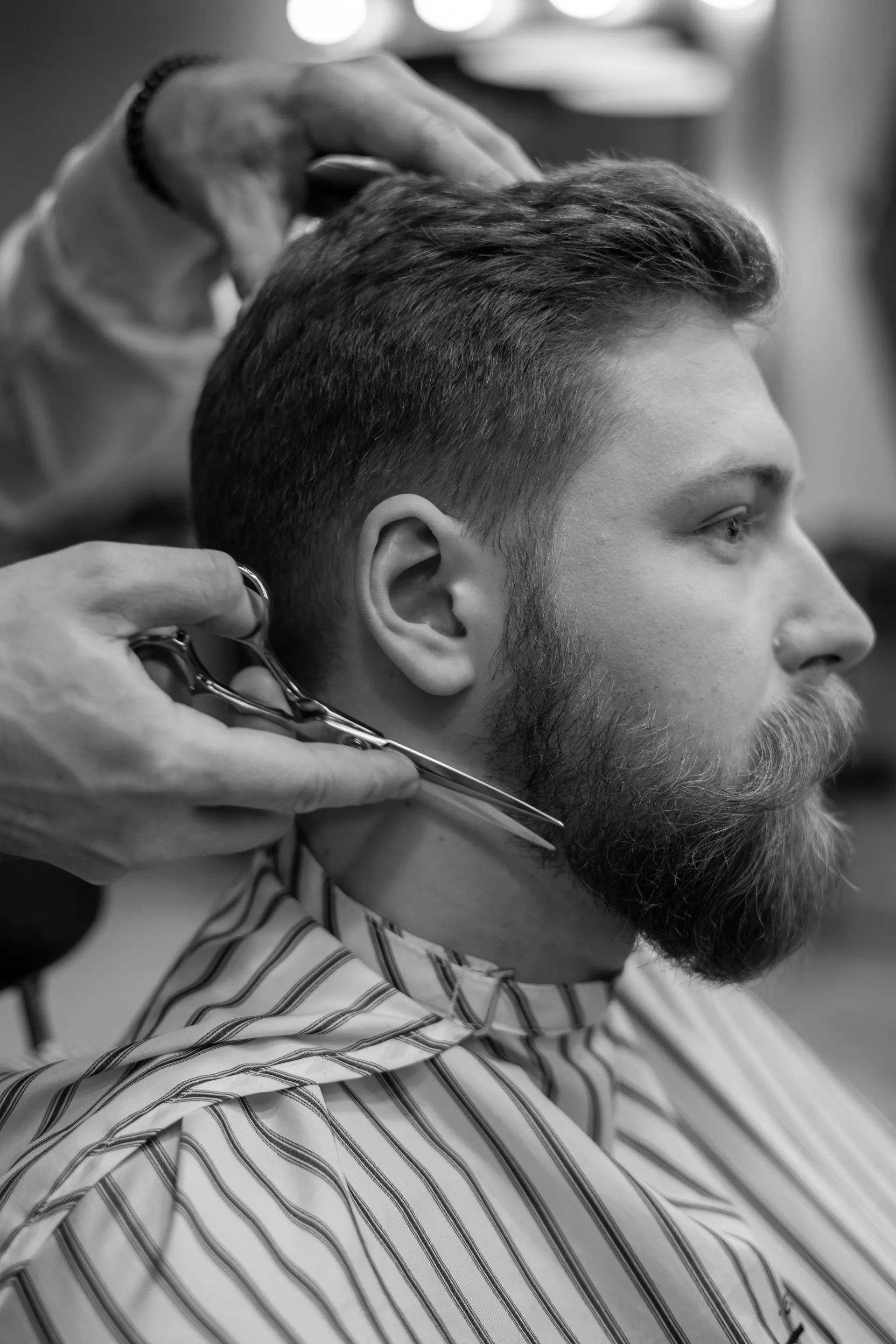 Um homem com barba está cortando o cabelo por um barbeiro.