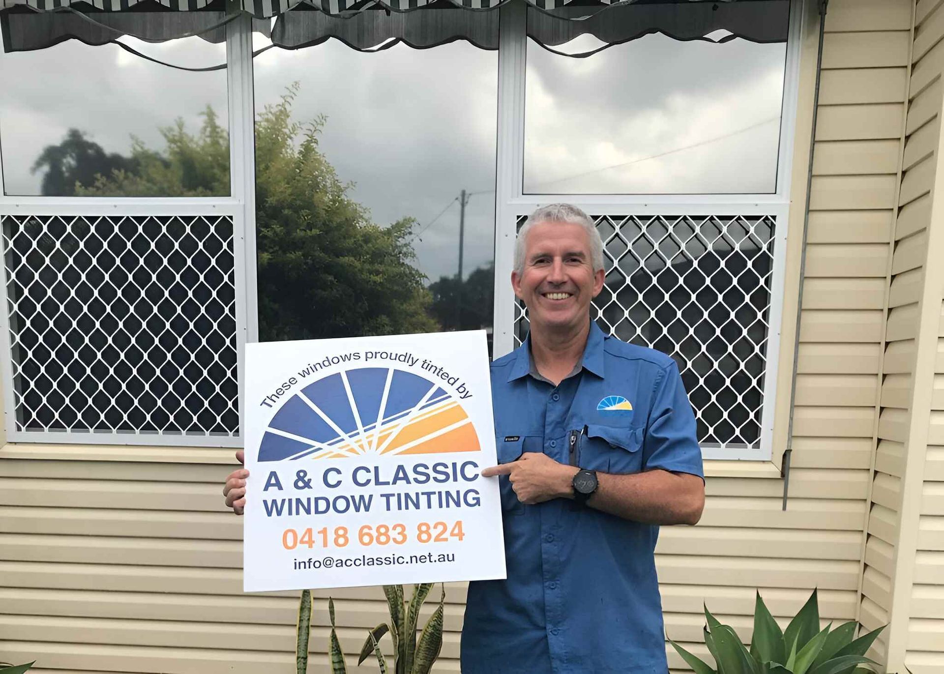 A Man Is Holding A Sign In Front Of A Window — A & C Classic Window Tinting In Wallsend, NSW