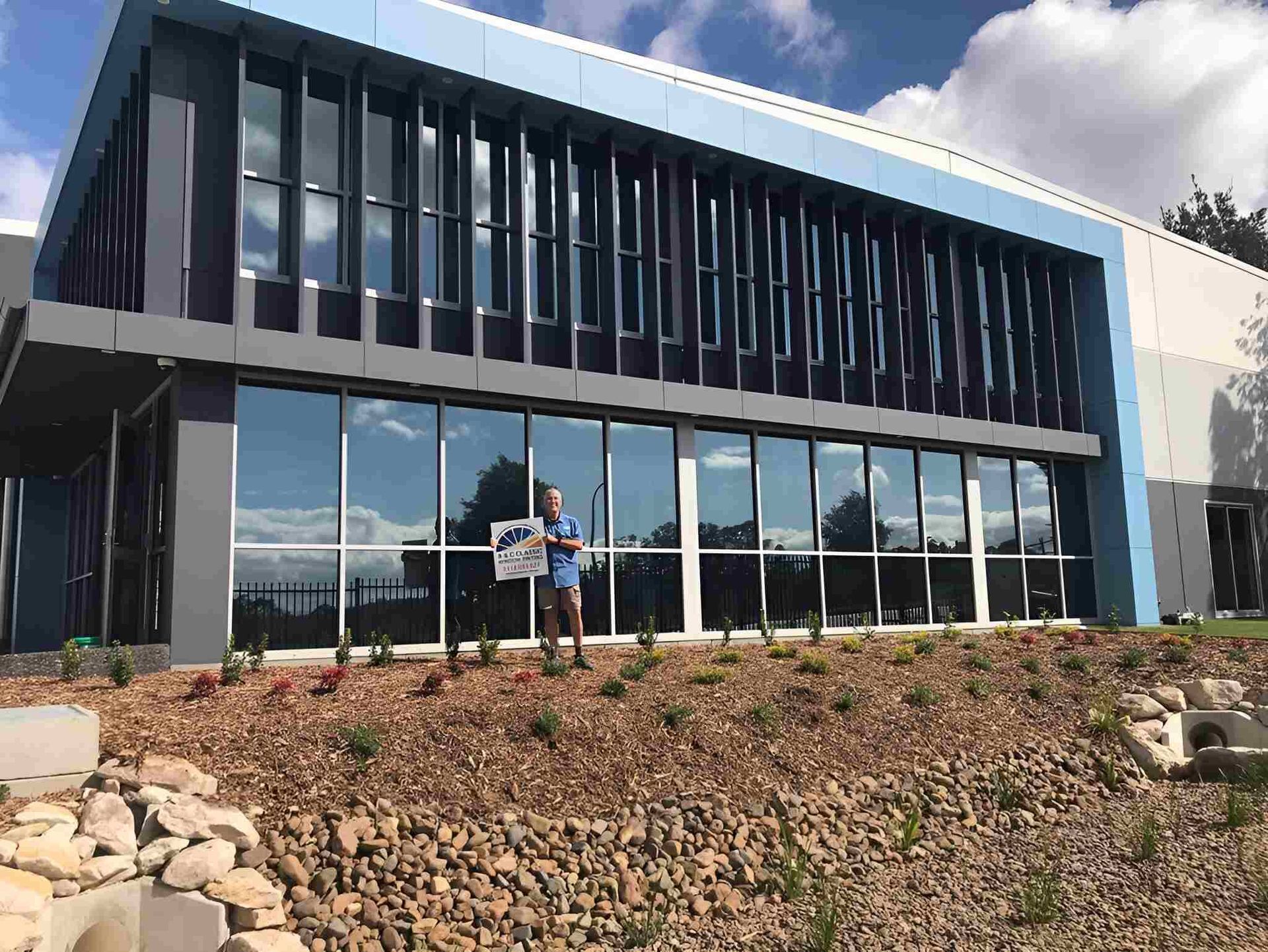 A Man Is Standing In Front Of A Large Building — A & C Classic Window Tinting In Maitland, NSW