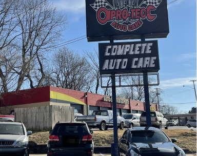A Pro-Tecc Auto Care sign stands above an auto repair shop with several parked cars on a sunny day | Pro-Tec Auto Care