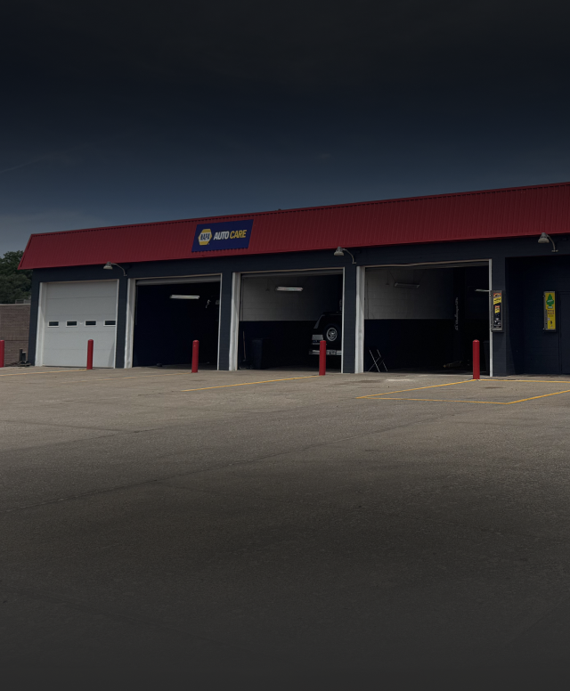 A low-angle view of an automotive service center with three open garage bays and a red roof under a dark sky | Pro-Tec Auto Care