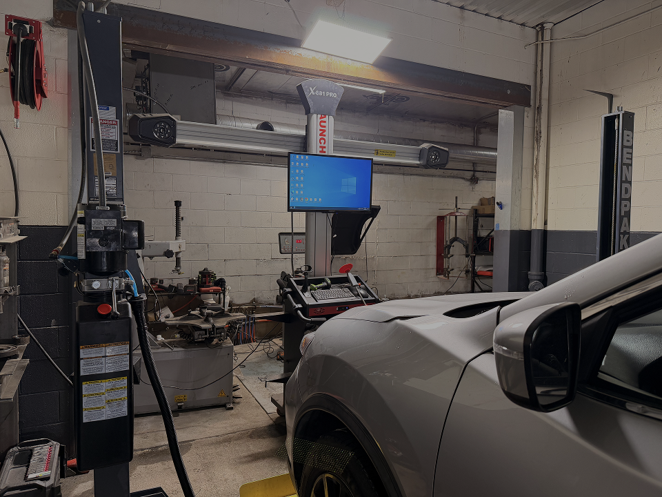 A car inside an automotive repair shop with a diagnostic computer screen and a tire machine in the background | Pro-Tec Auto Care