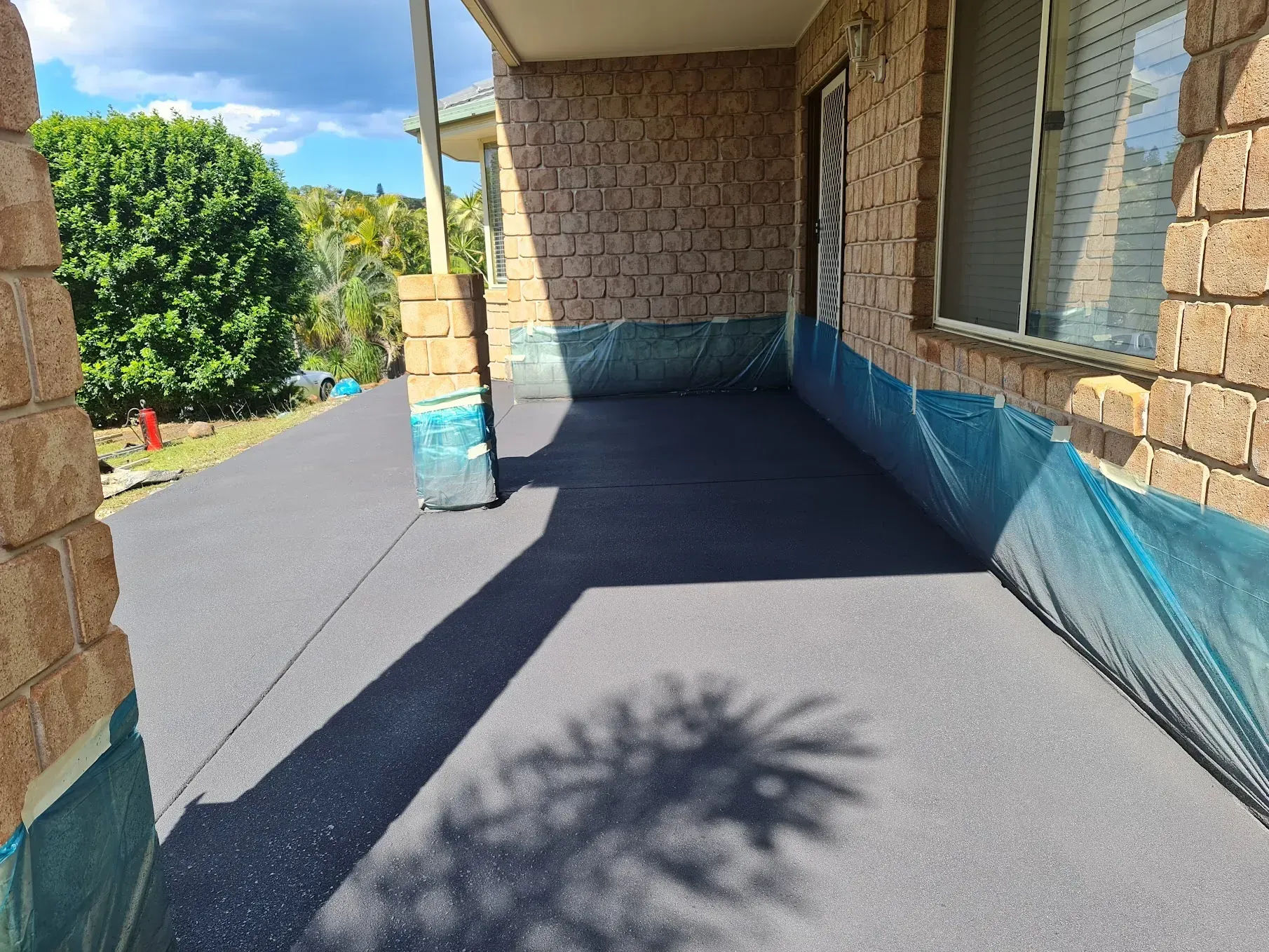 A driveway with a small boat on a trailer, with trash cans and a garage.
