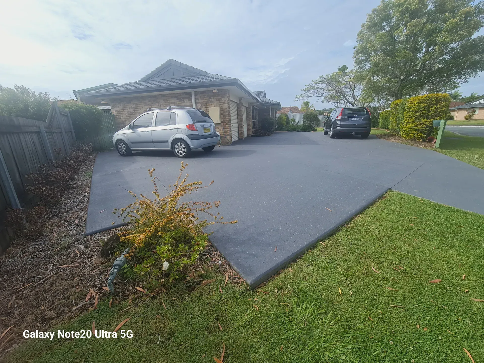 A silver car parked in a driveway in front of a brick building. Black car parked at the end of the driveway.