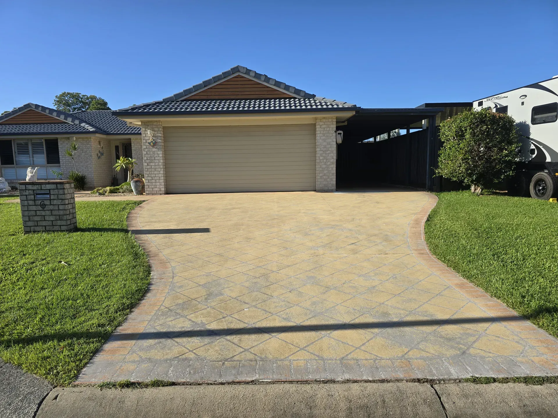 Two-story house with two garage doors, brown brick exterior, and blue sky. Asphalt driveway.