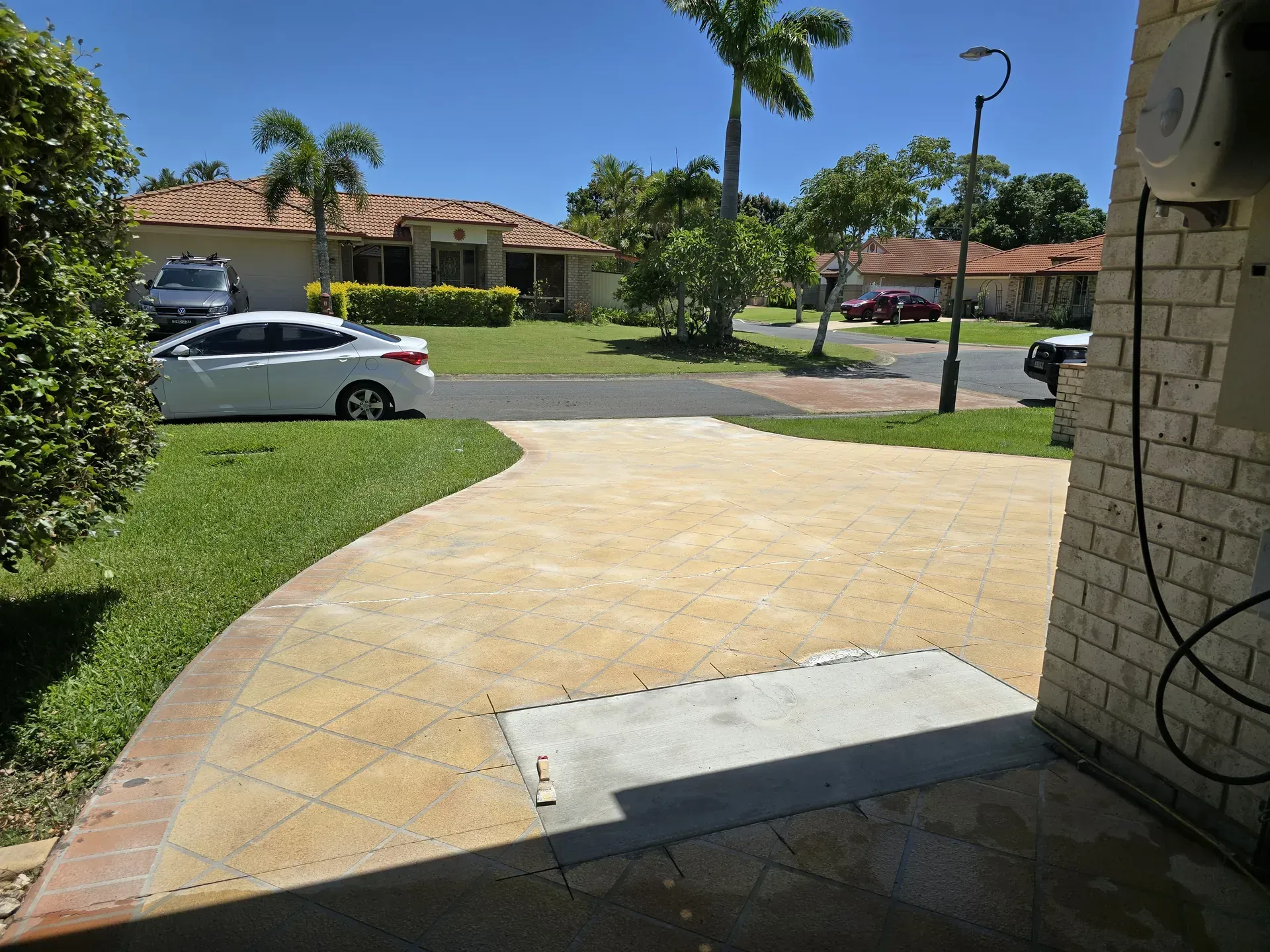 Driveway with tan pavers, grass, a white car, and houses on a sunny day.