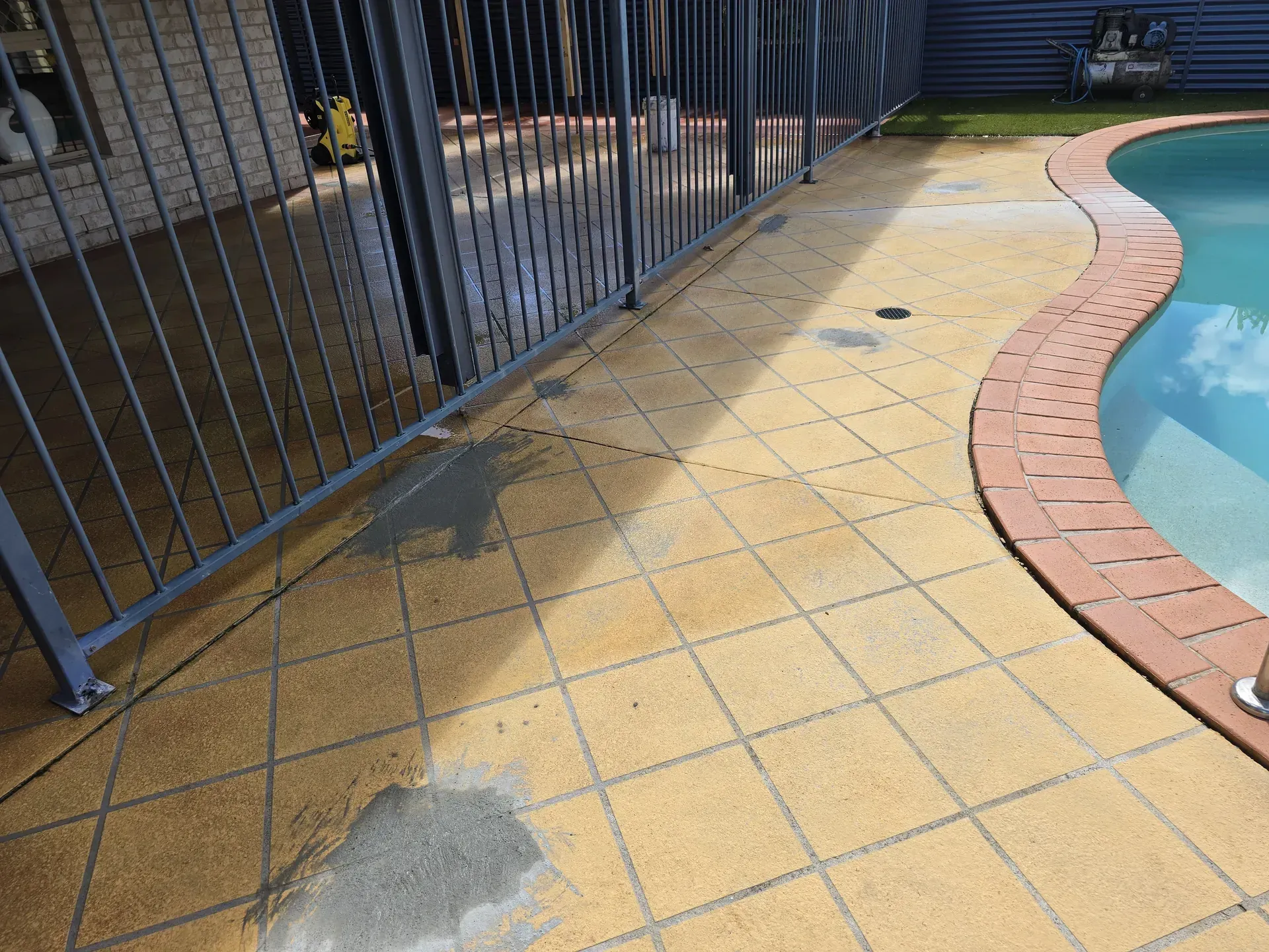 A beige concrete driveway leads to a house with a wooden deck, stairs, and an air conditioning unit.