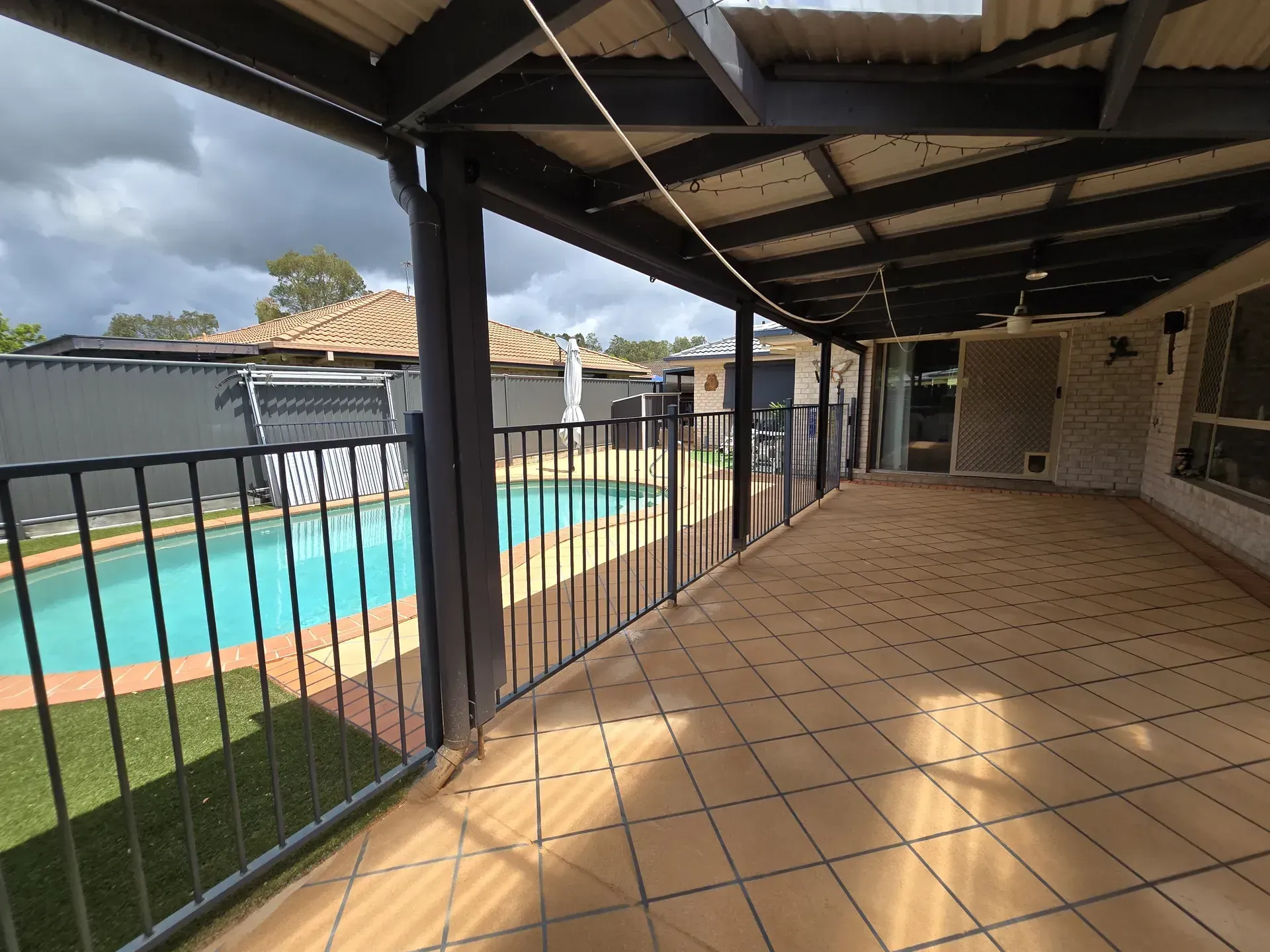 Covered patio overlooking a backyard with a swimming pool. The sky is overcast.