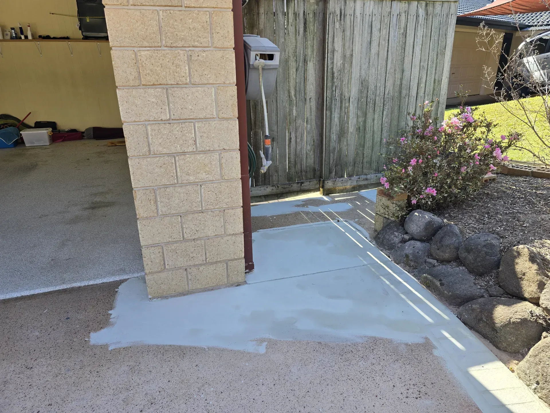 Concrete driveway with a newly applied gray patch, leading to a weathered wooden gate and brick column.