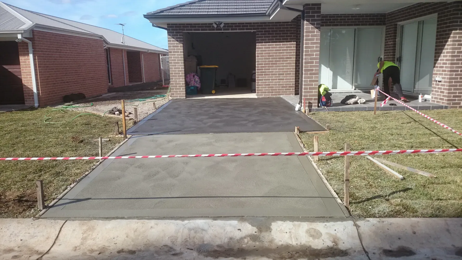 Concrete driveway and sidewalk under construction at a house. Red and white tape blocks off areas.