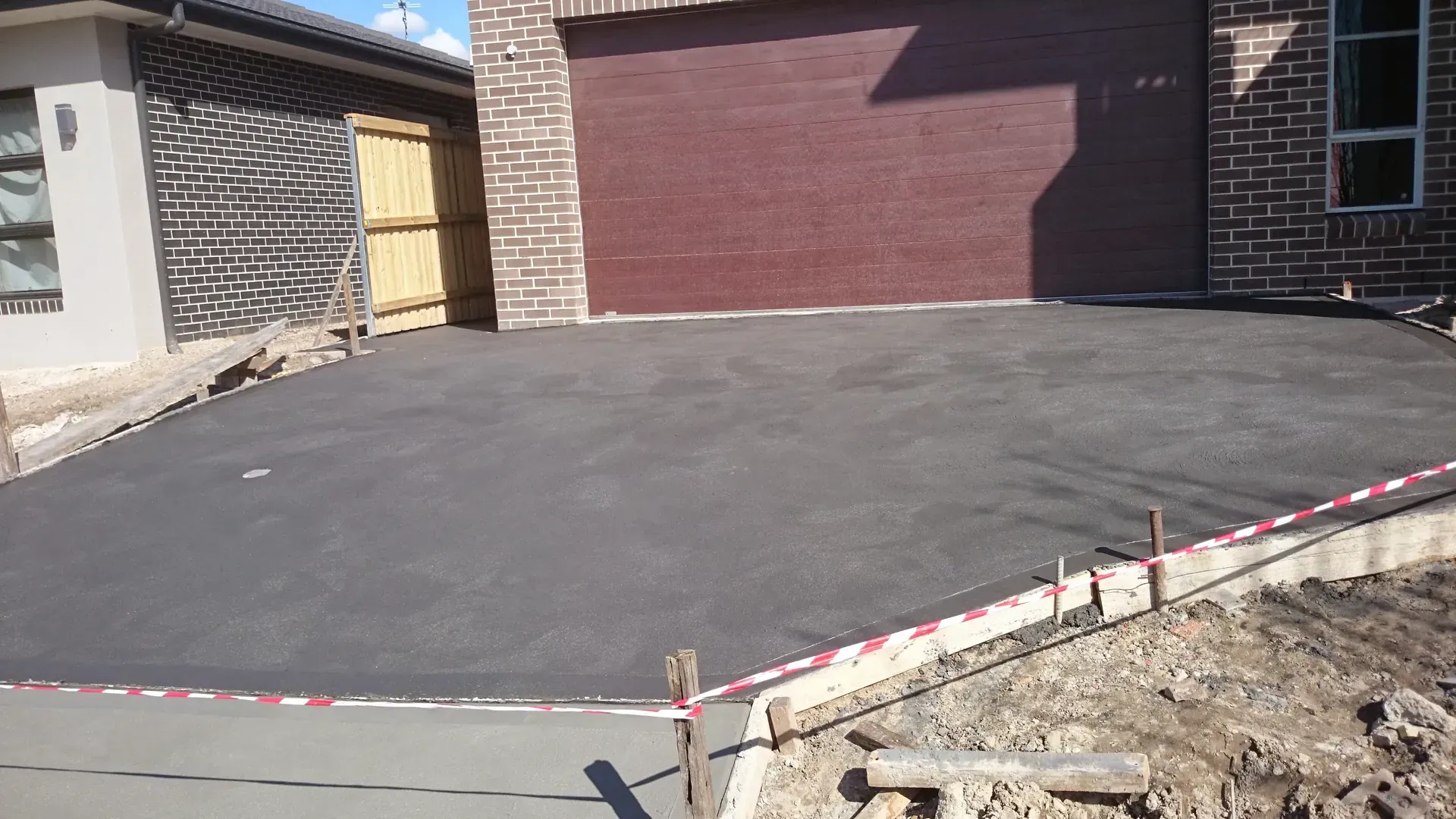 Newly poured asphalt driveway in front of a brick garage and house.