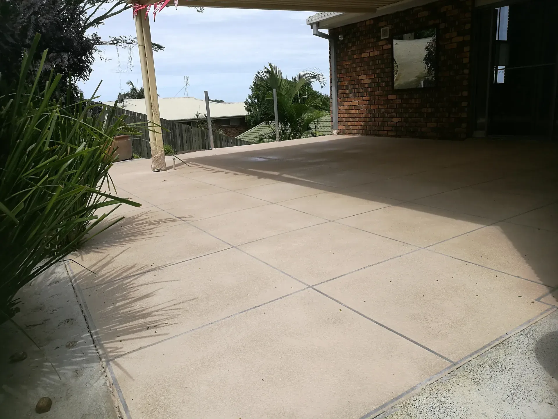 Concrete patio with a basketball hoop, beneath a brick-walled structure, with a view of a neighborhood.