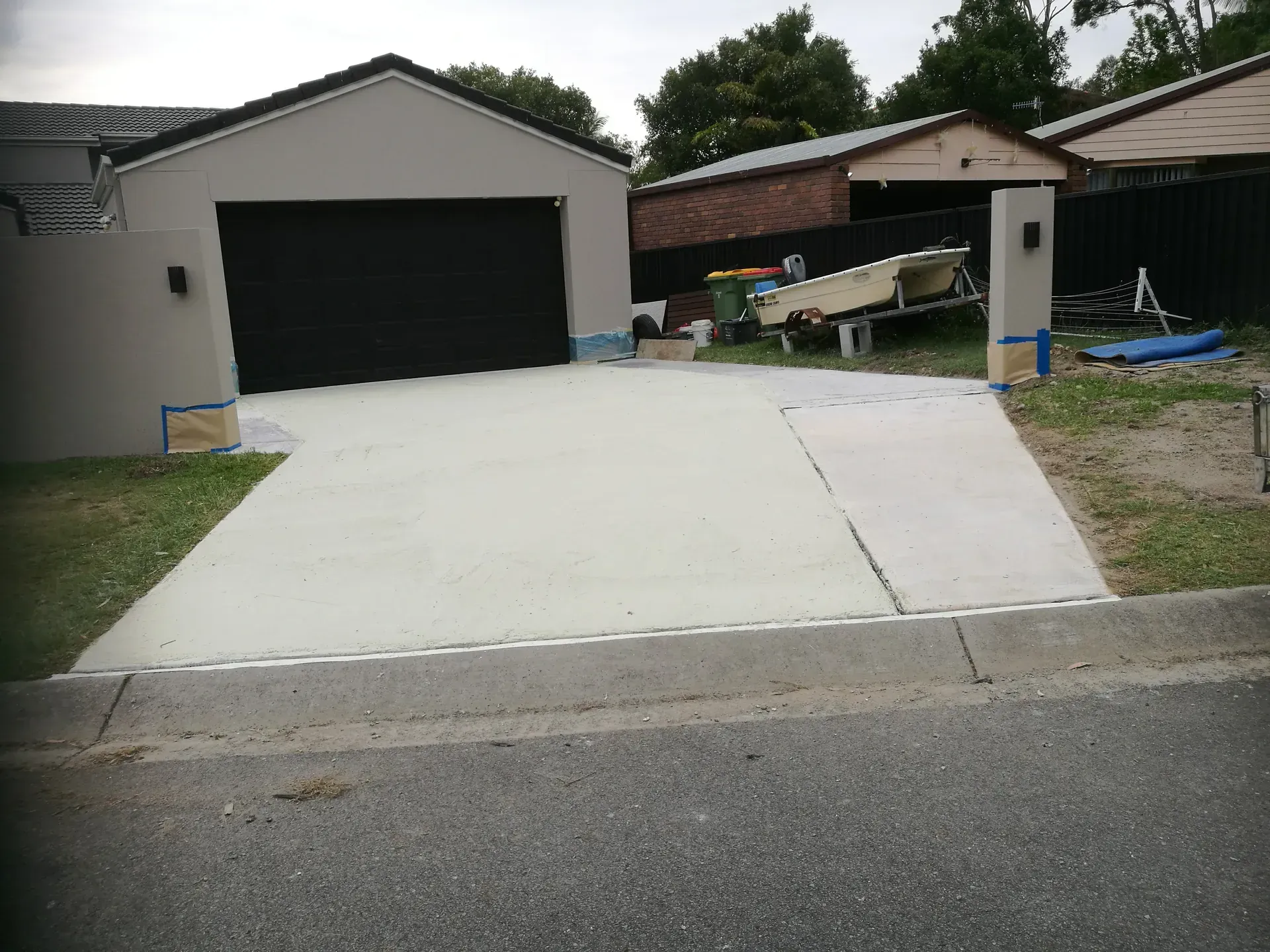 Gray driveway with two cars parked, front of a beige house and green grass.