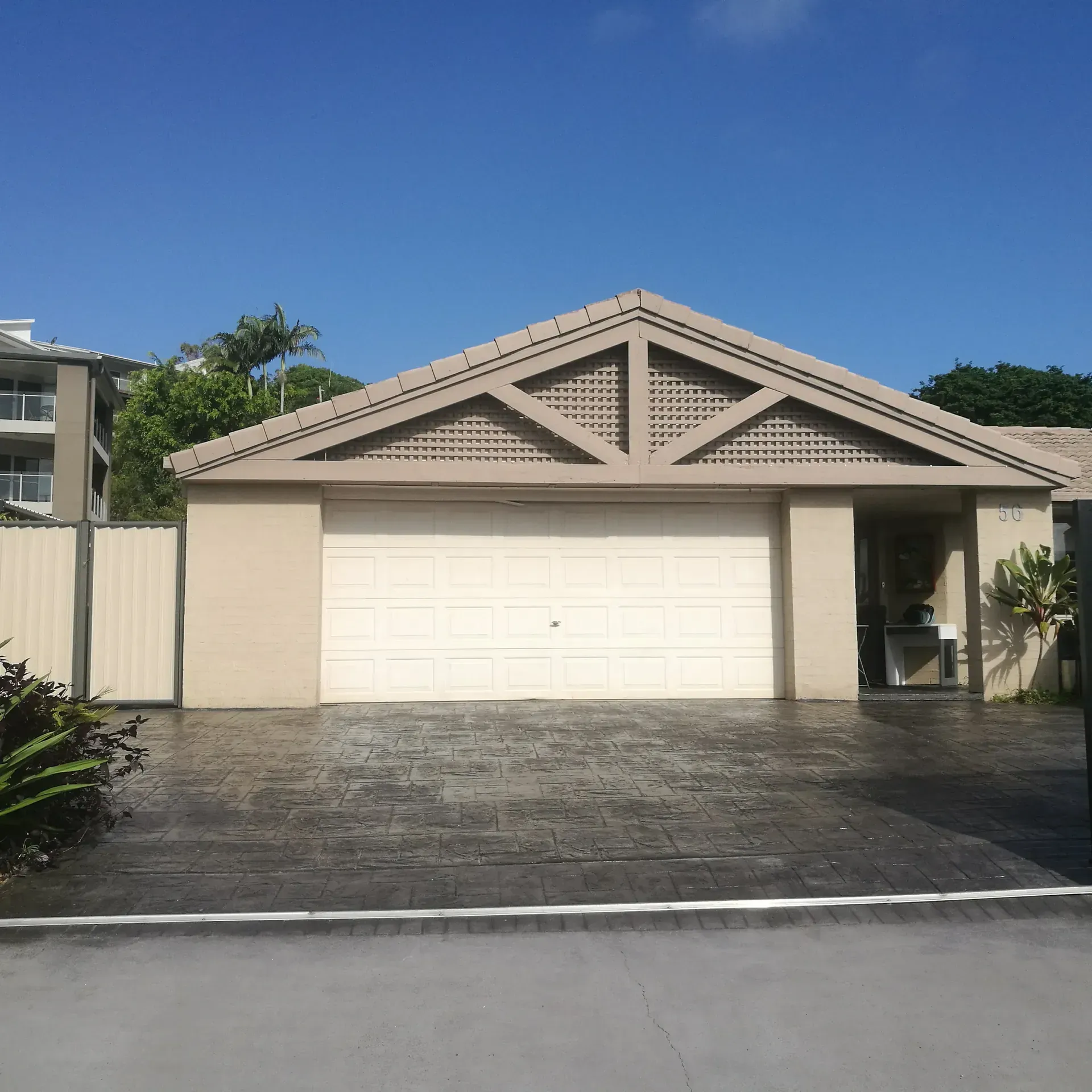 Tan garage with a decorative wooden triangle above the door, driveway, and blue sky.