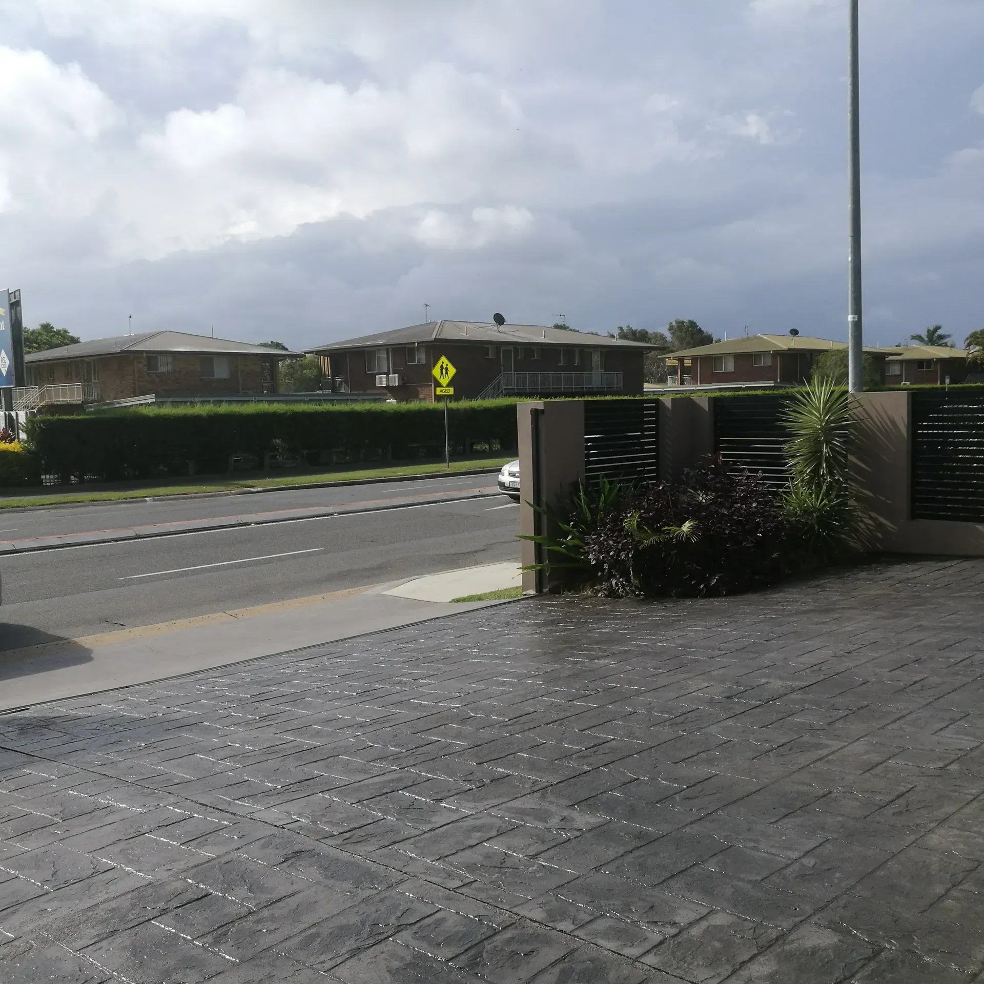 Dark gray driveway with cracks, drain, and building on the left side.