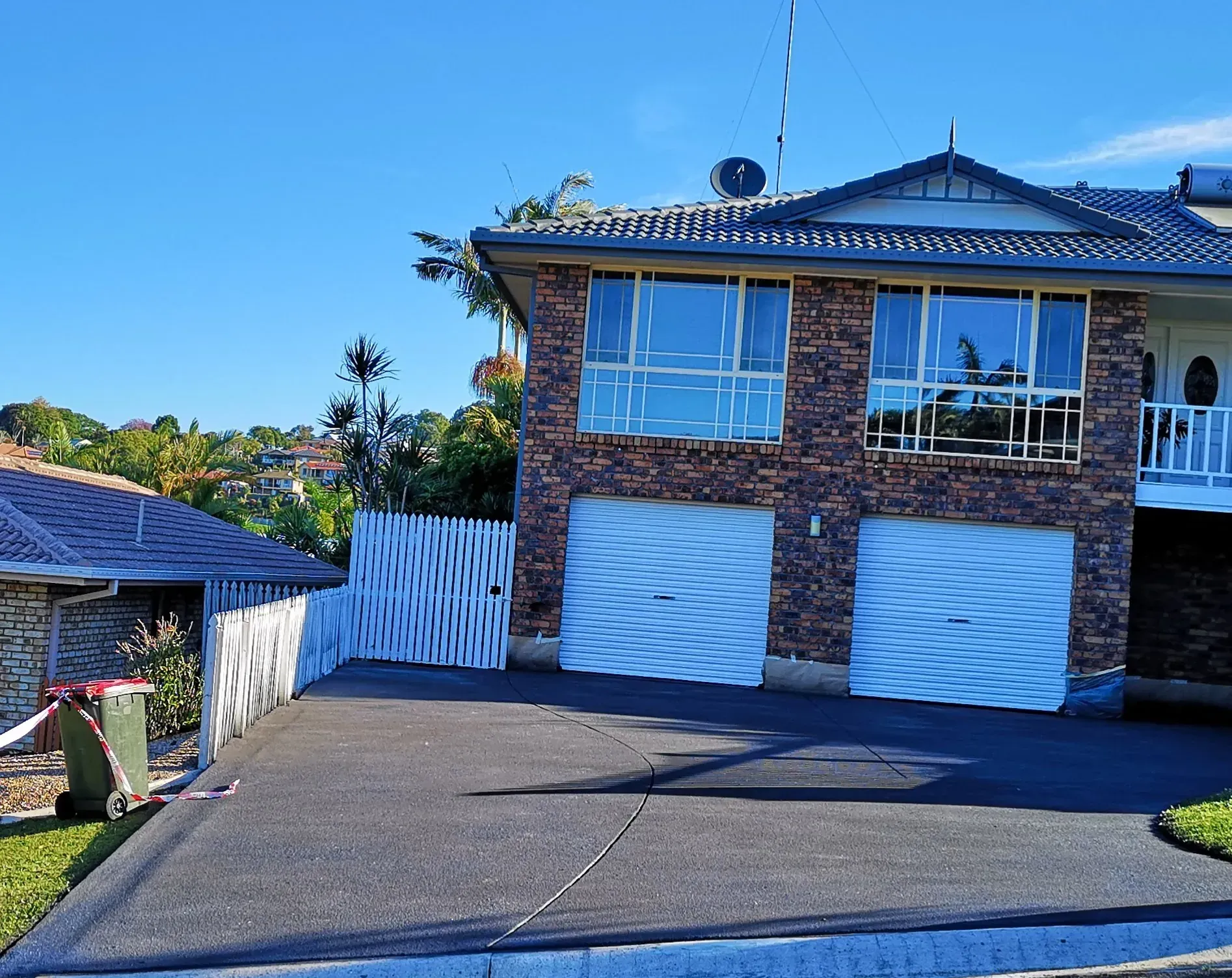 Two-story brick house with two garage doors and a paved driveway under a blue sky.