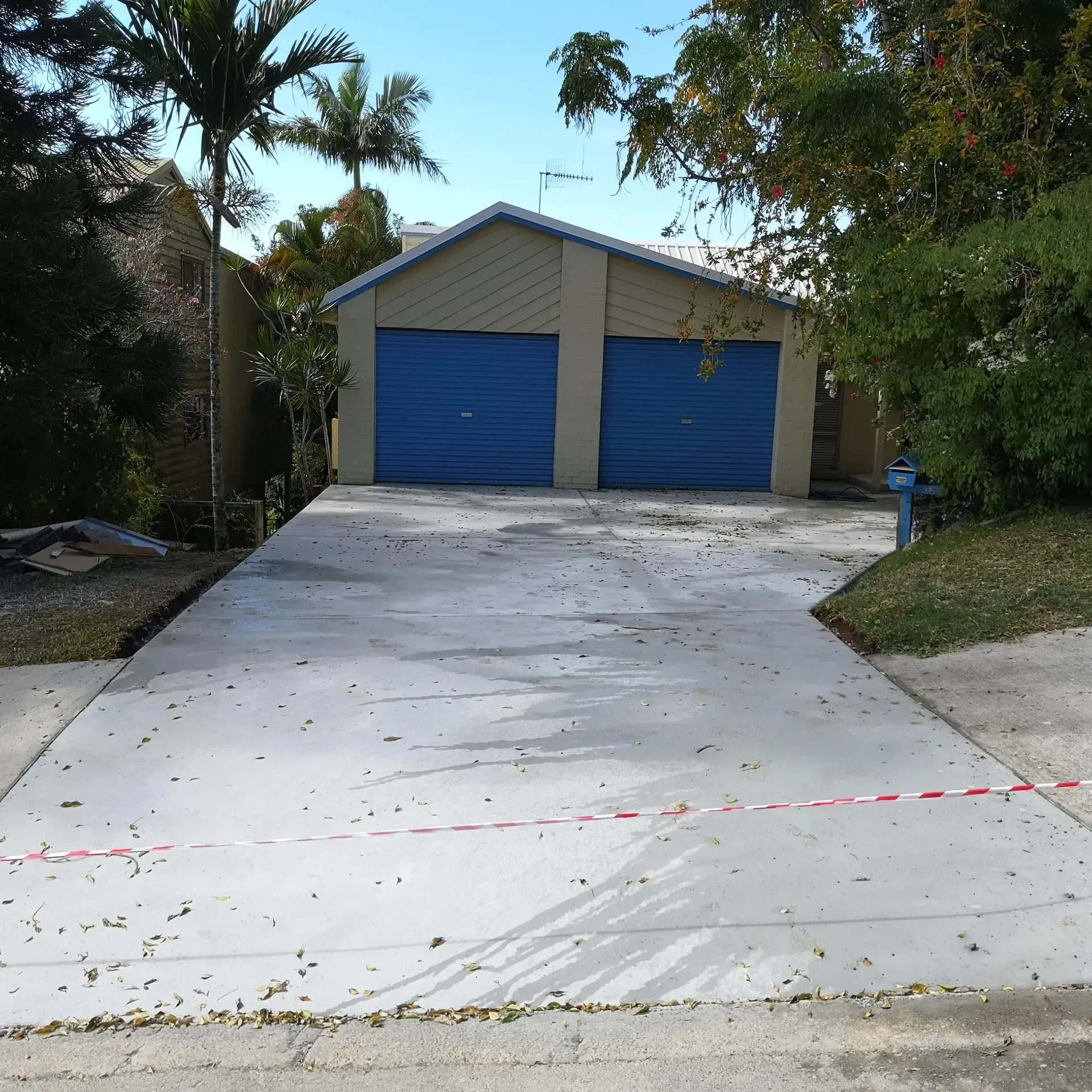 Street view: Houses in the background, road, fence with plants, cloudy sky.