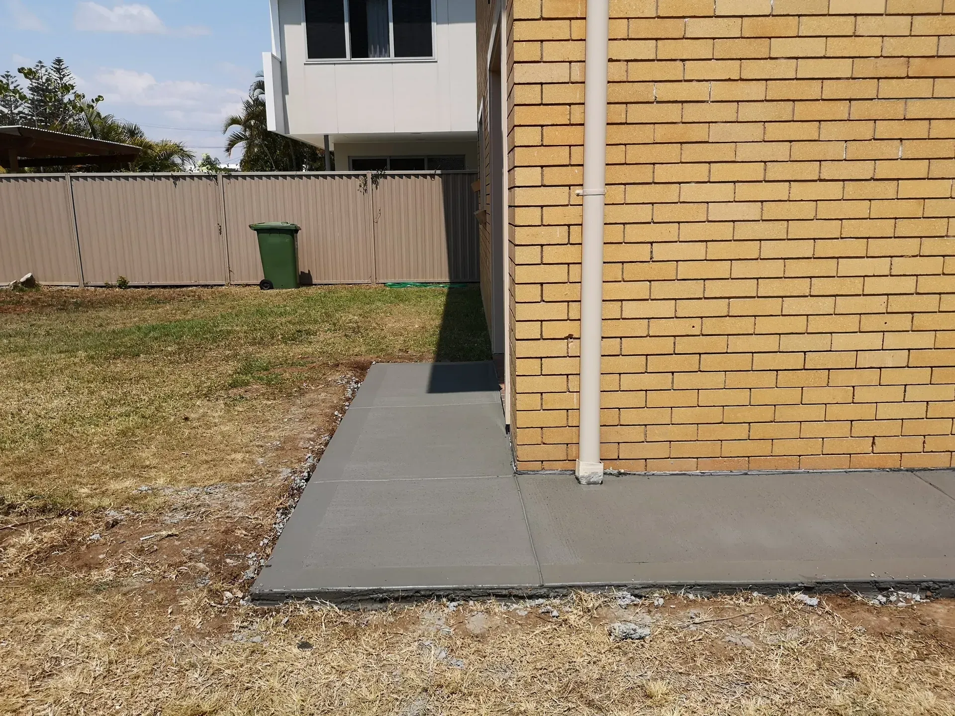 Concrete walkway beside a yellow brick wall. A green trash can sits in the background.