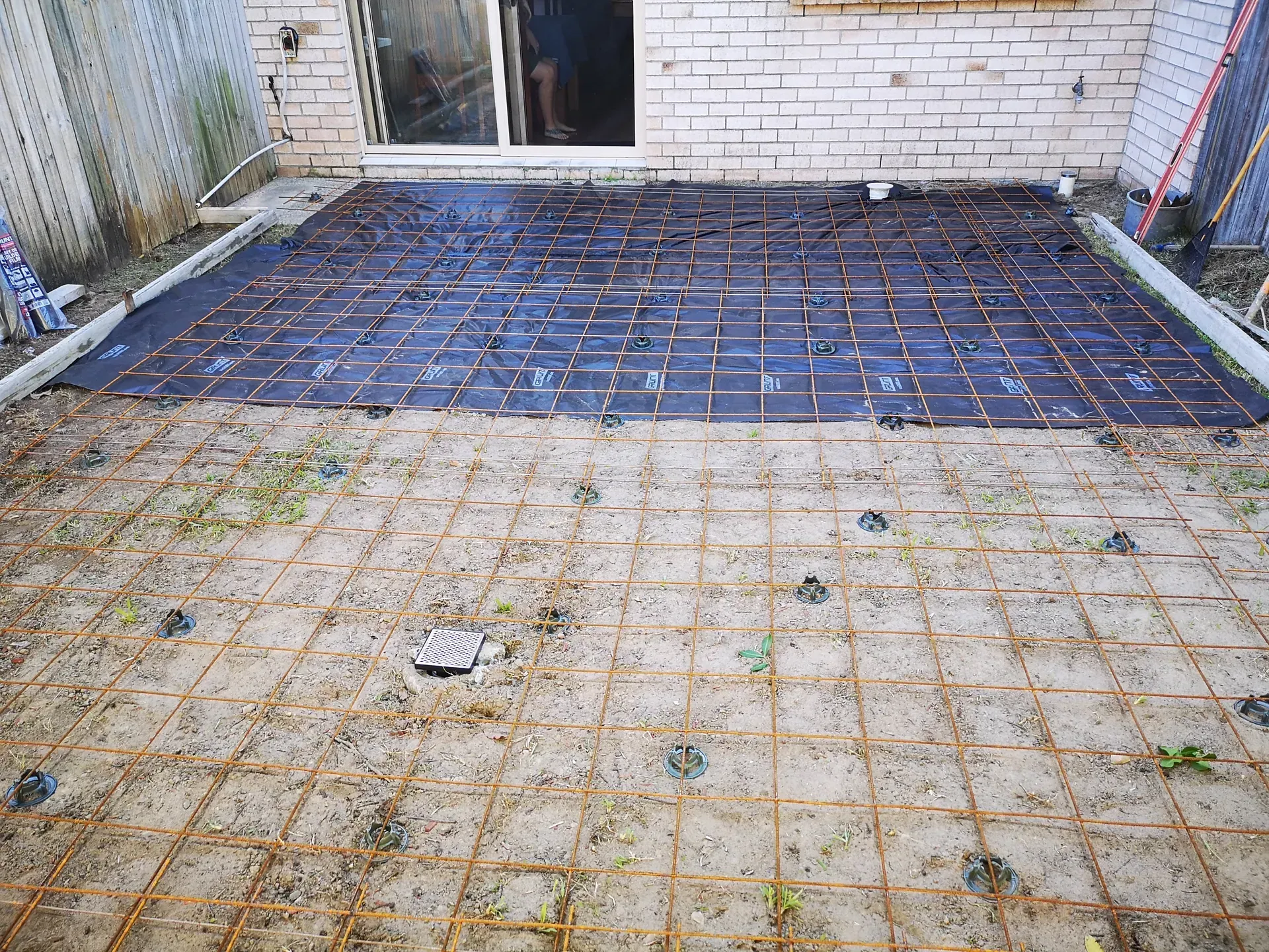 Patio area with prepared ground for concrete; wire mesh and black material are laid out.