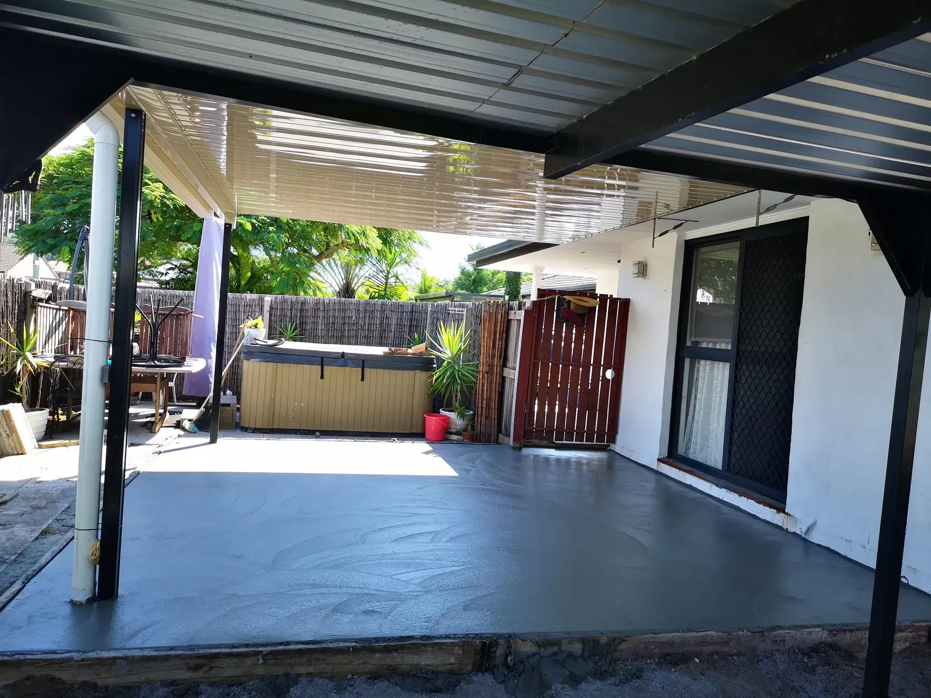 Stamped concrete patio, wet and reflective, with a metal table and partial view of a fence.
