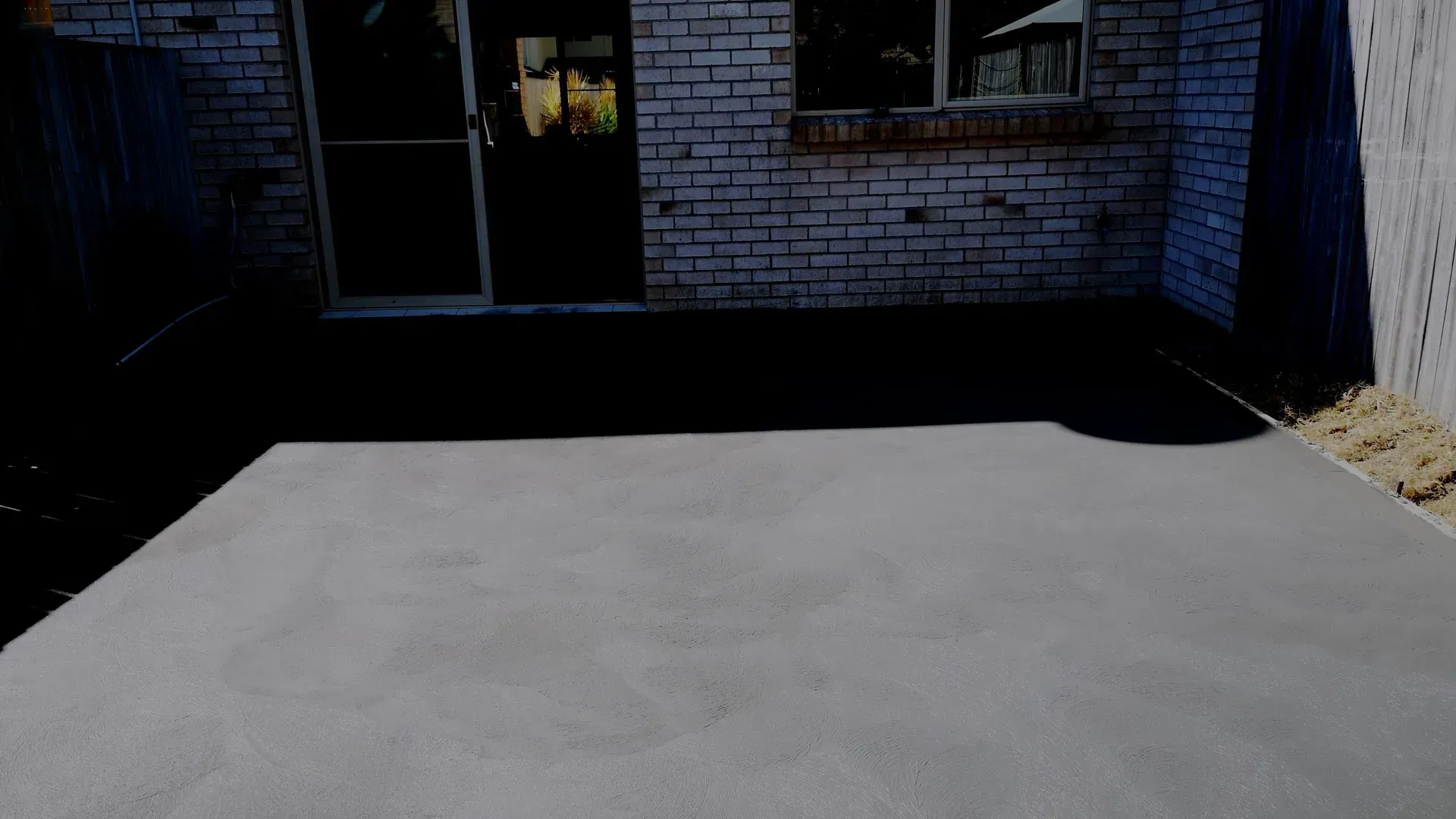 Gray concrete patio in front of a brick building with a glass door and window.