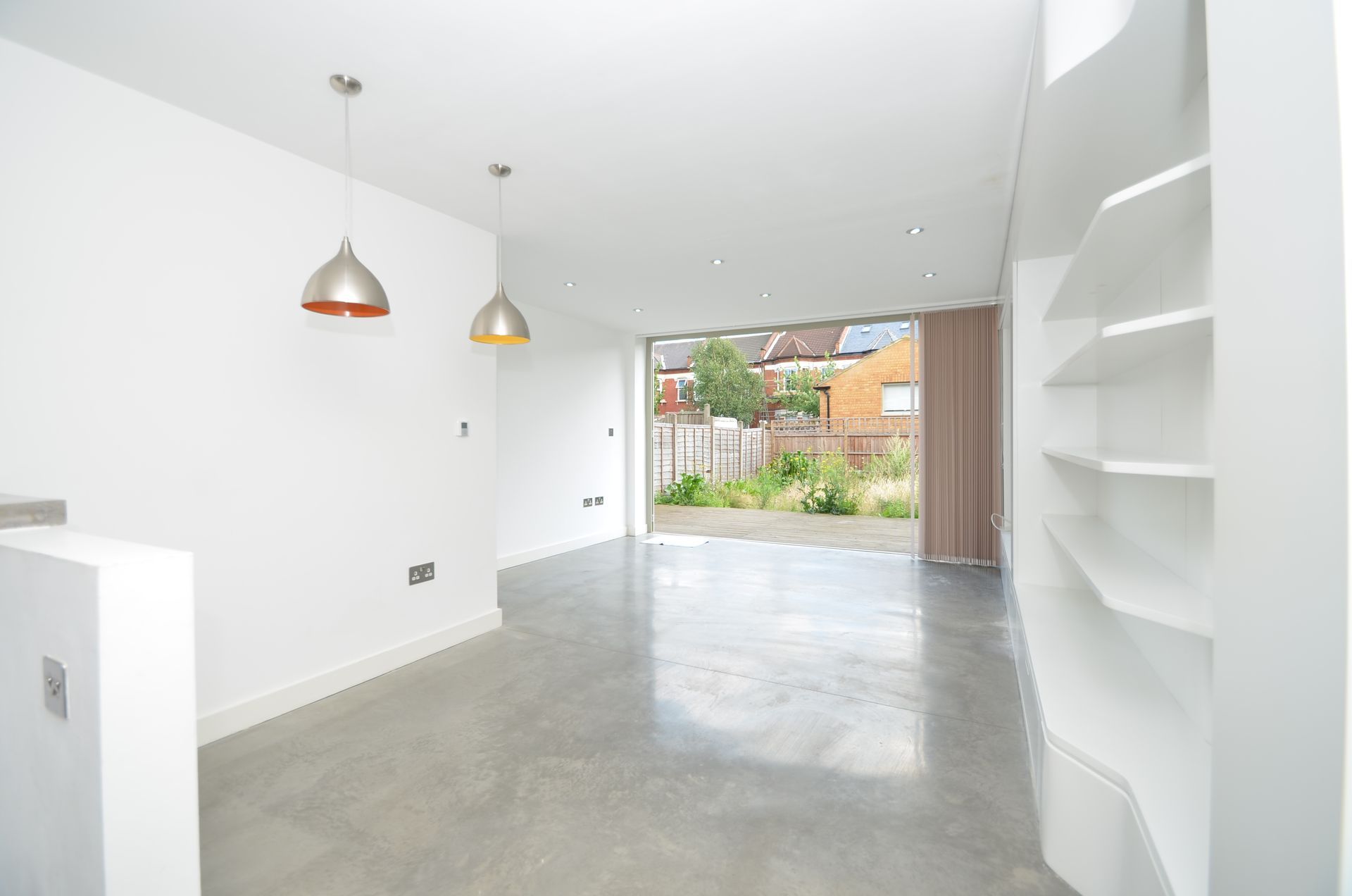 Bright white modern room with concrete floor, open to a garden. Two pendant lights hang.