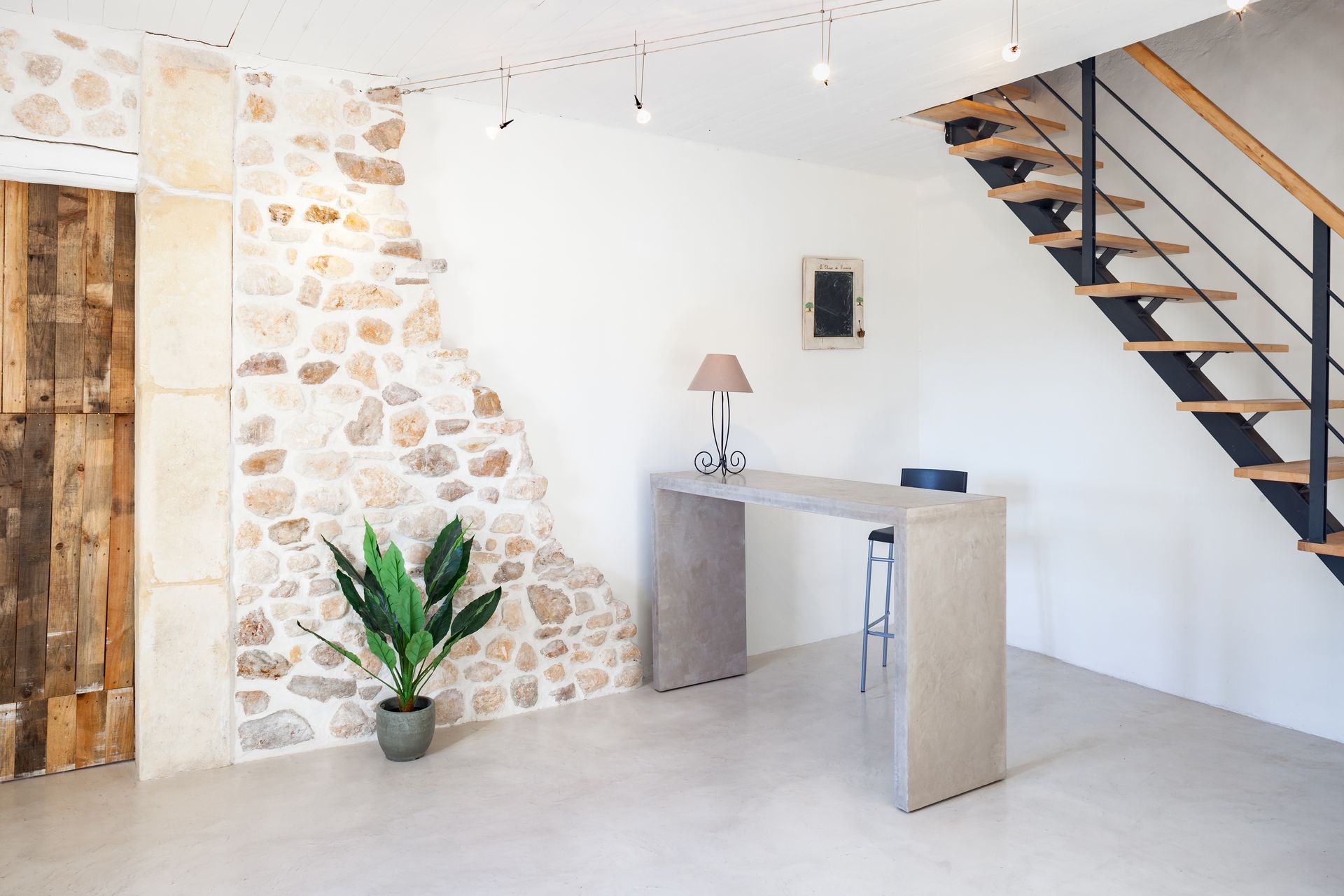 Interior with stone wall, wooden door, floating stairs, concrete desk, and a potted plant.