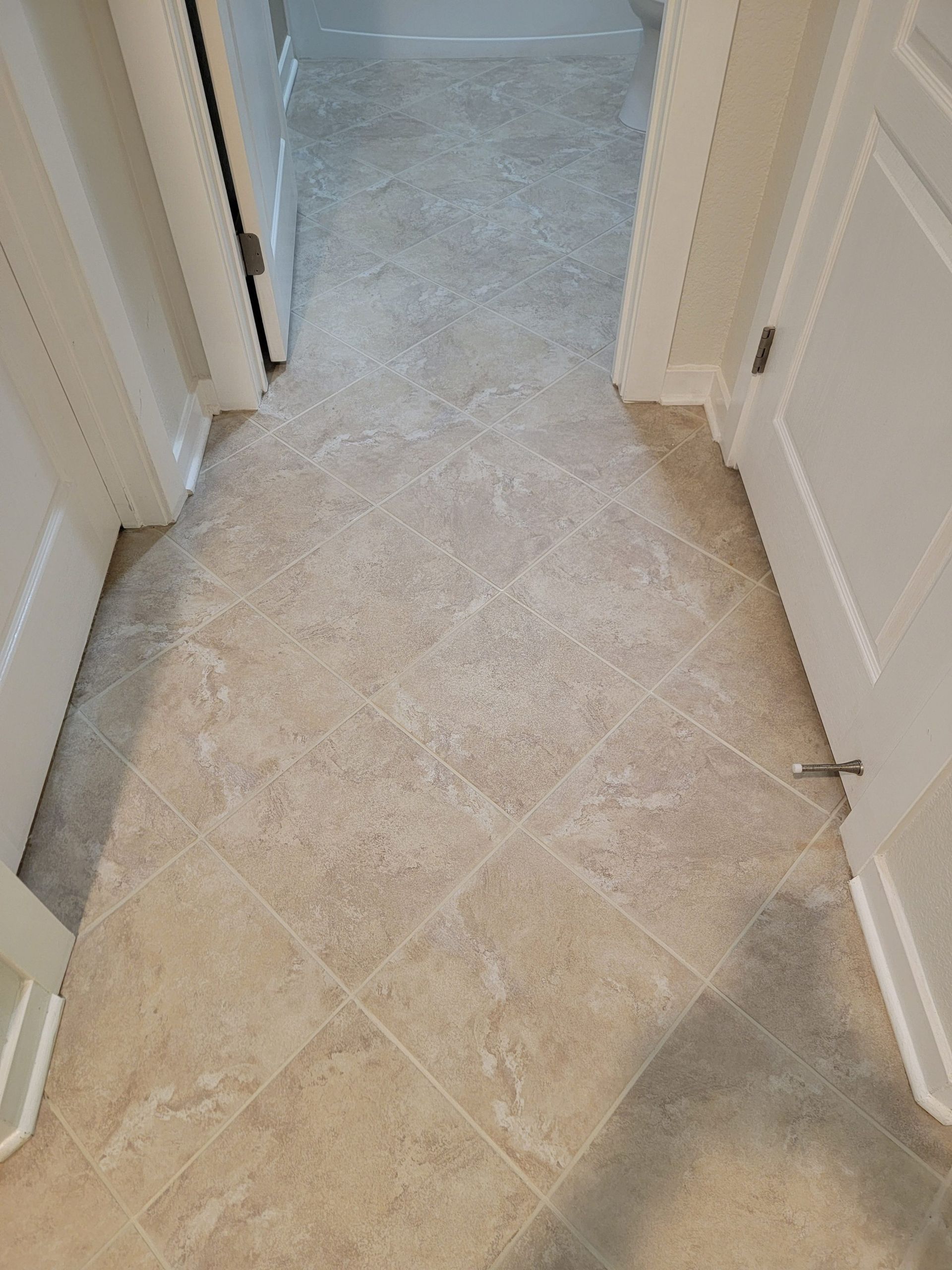 Narrow hallway with beige tile floor, white doors, and carpet edges along the sides