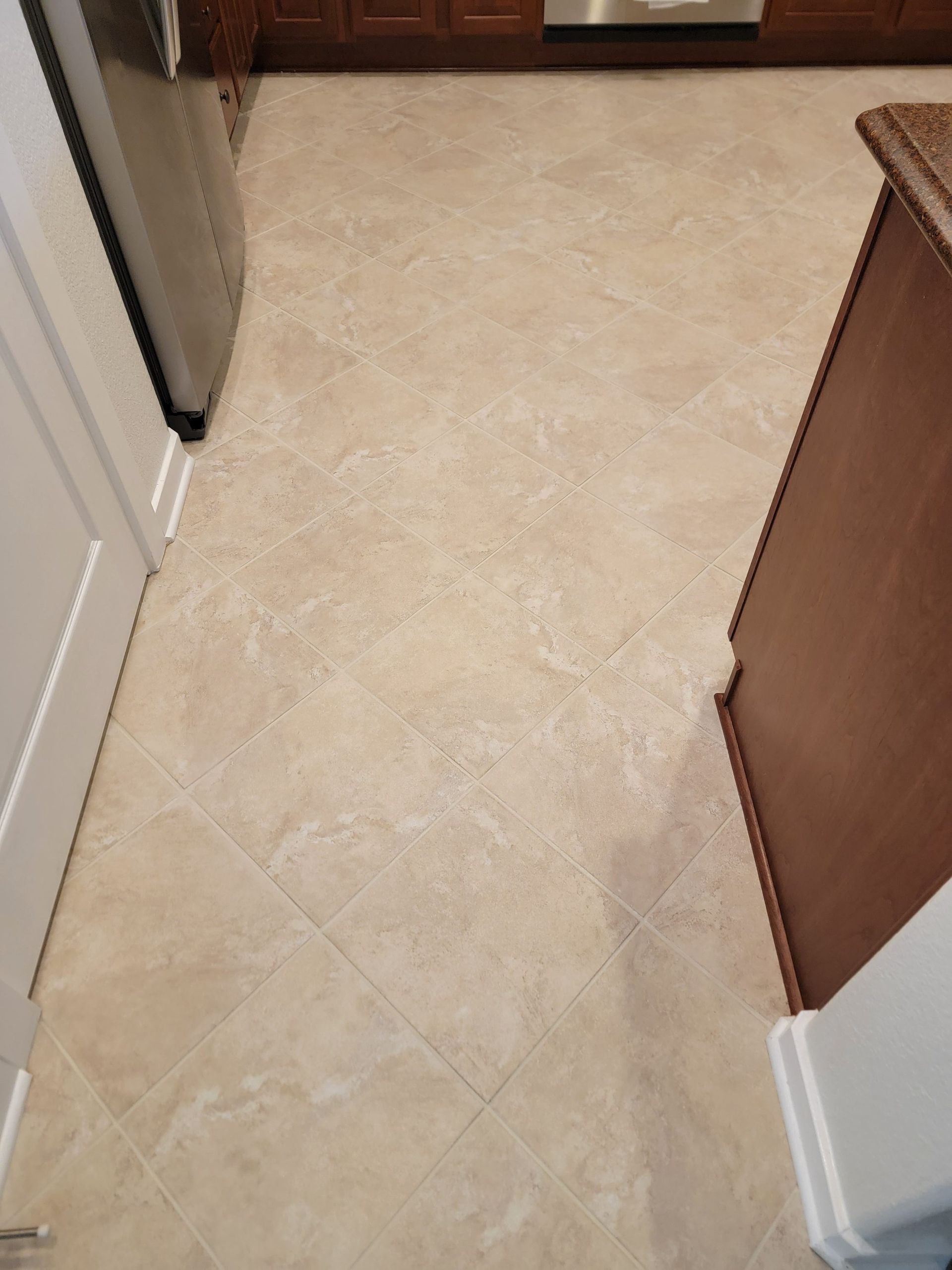 Kitchen floor with beige tile between a white fridge and wooden cabinets